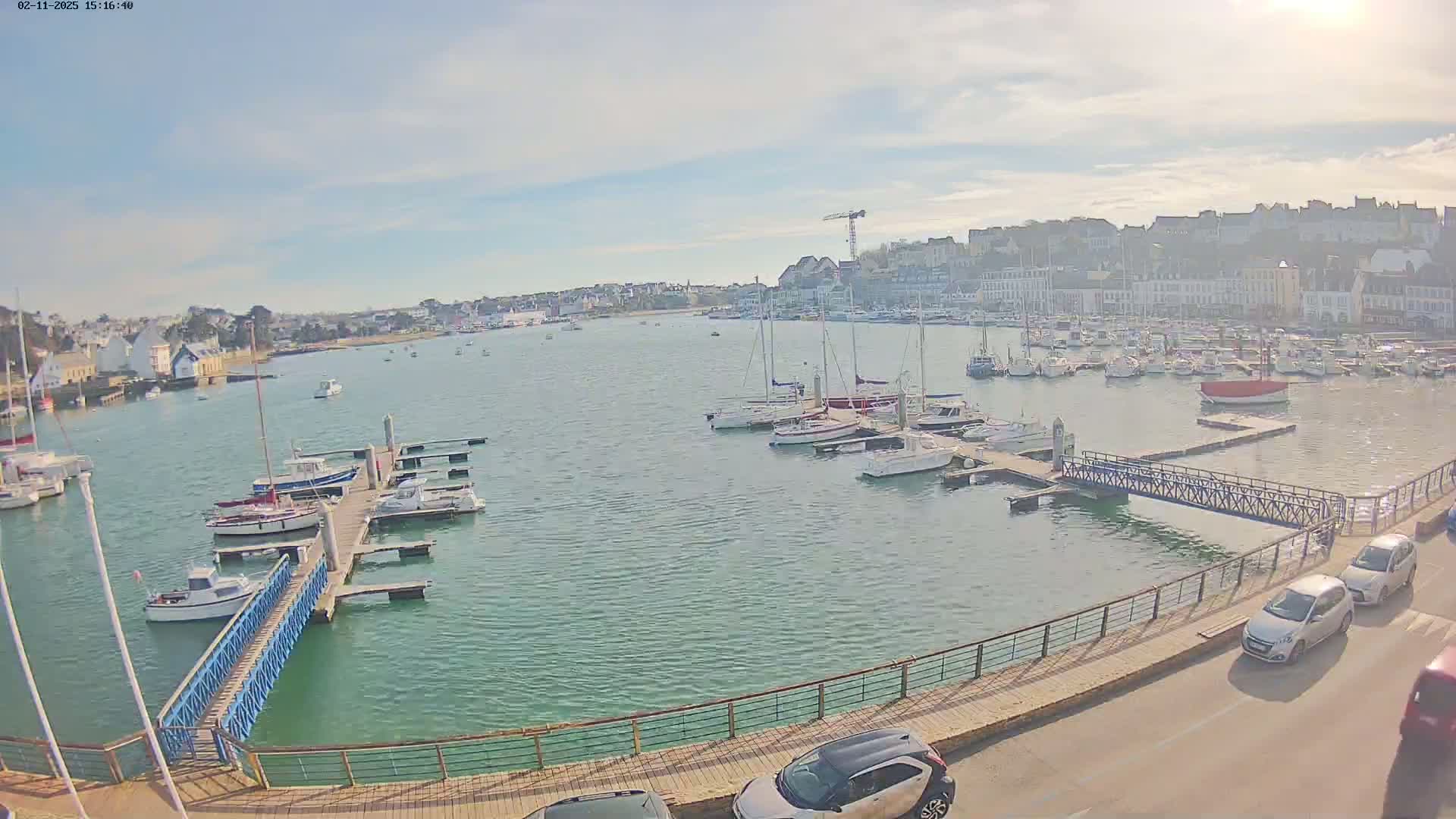 A harbor filled with numerous boats and yachts under a partly sunny sky, with a town and buildings visible in the background.