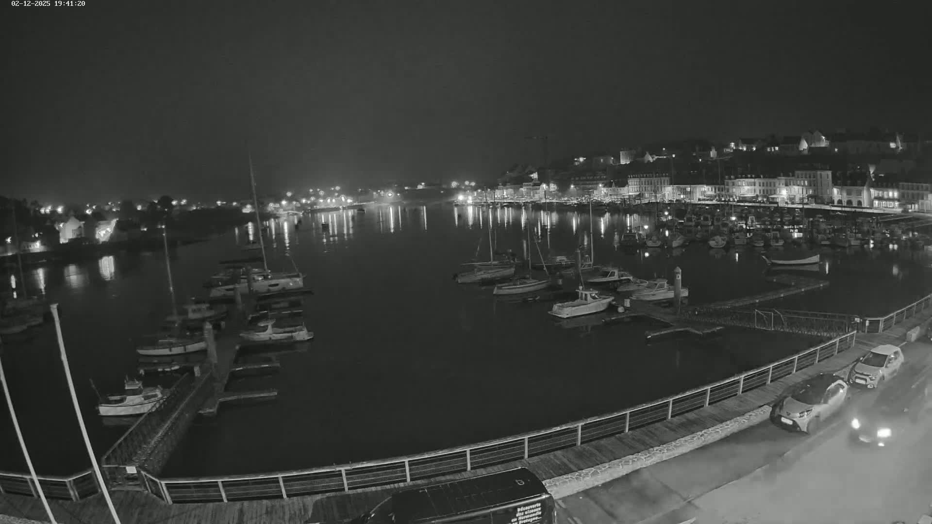 A nighttime view of a harbor filled with boats, docked alongside a waterfront town under a dark, overcast sky.