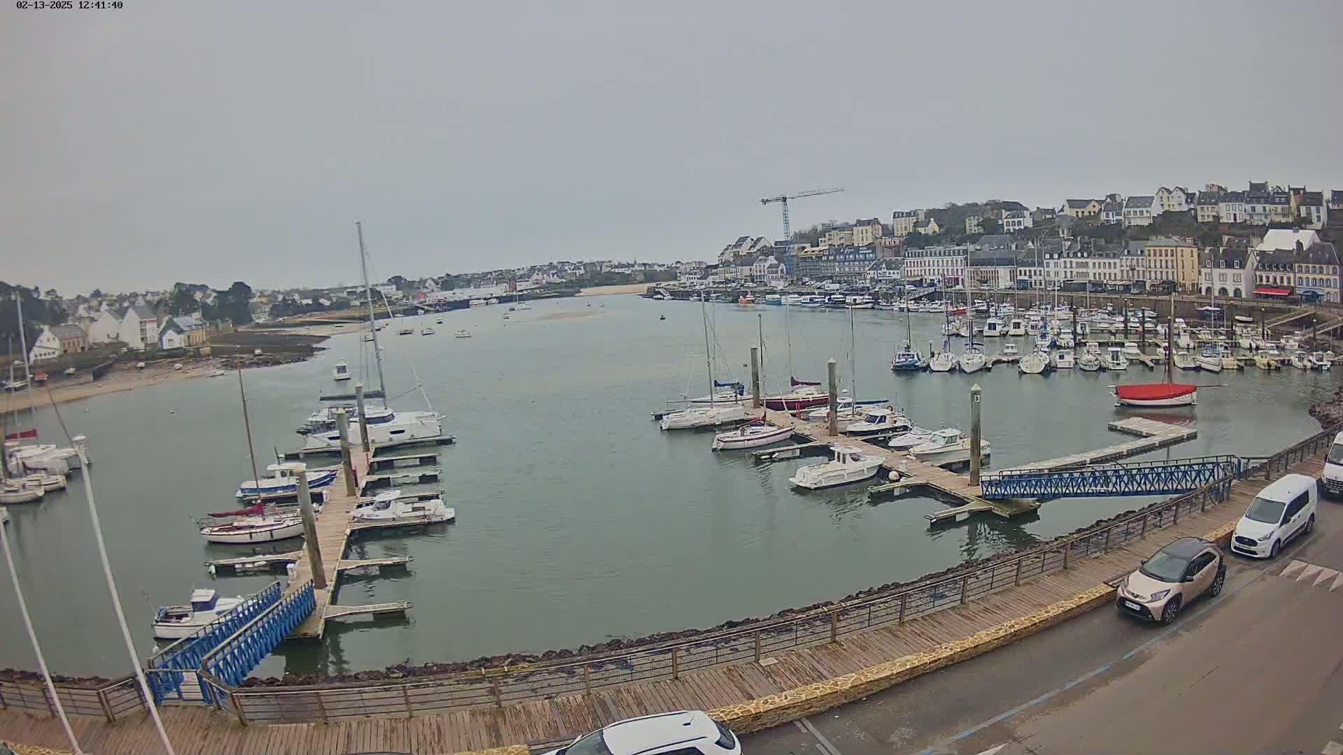 A harbor filled with numerous sailboats and motorboats on a cloudy day, with a town in the background.