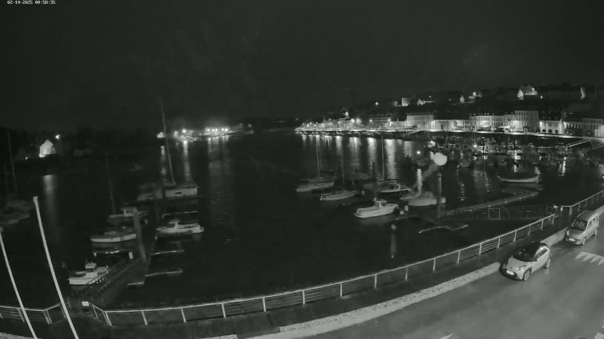 A nighttime view of a harbor filled with boats, next to a town with lights reflecting on the water.