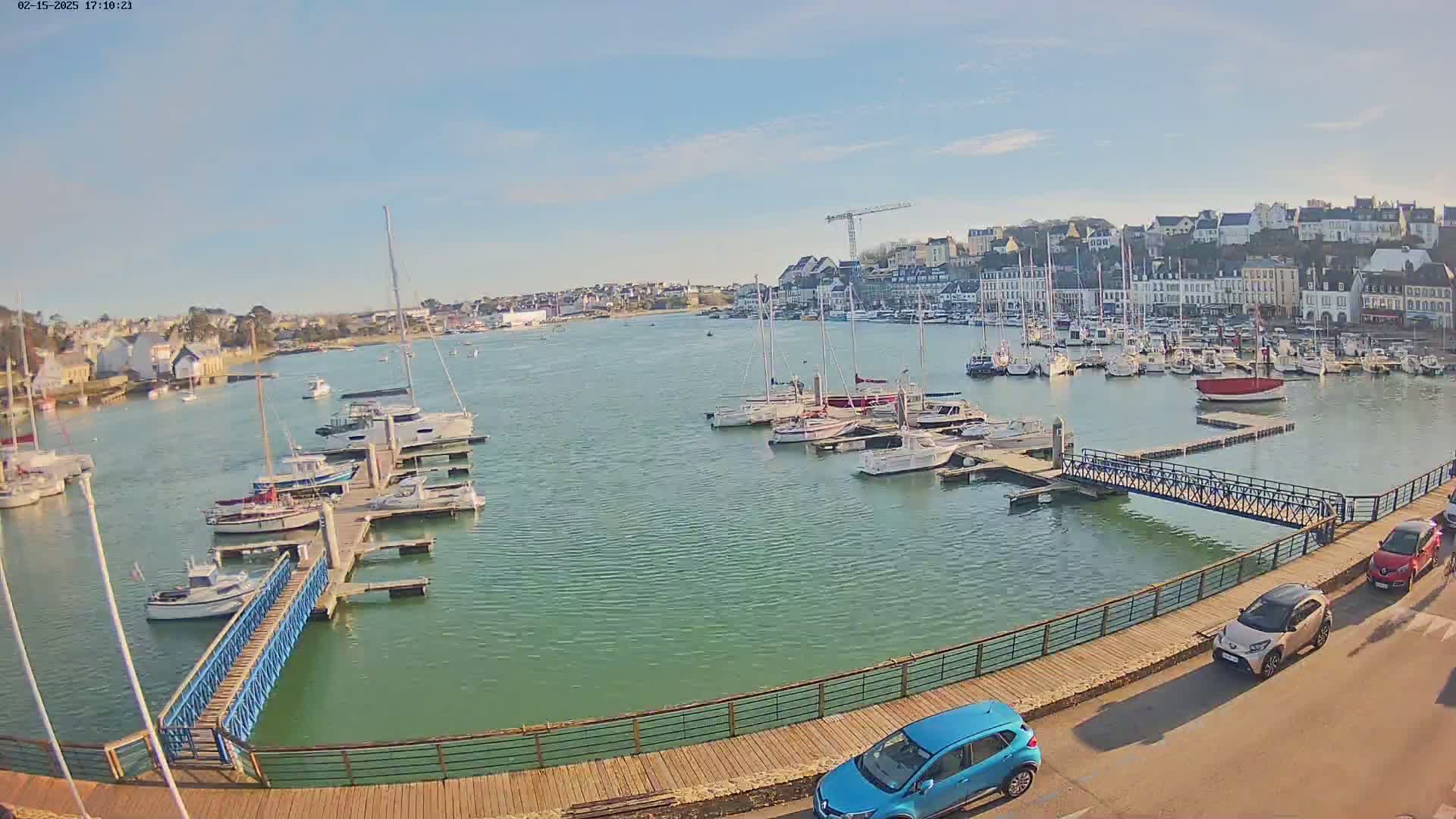 A harbor filled with numerous boats on a sunny day, with a town and a walkway visible in the background.