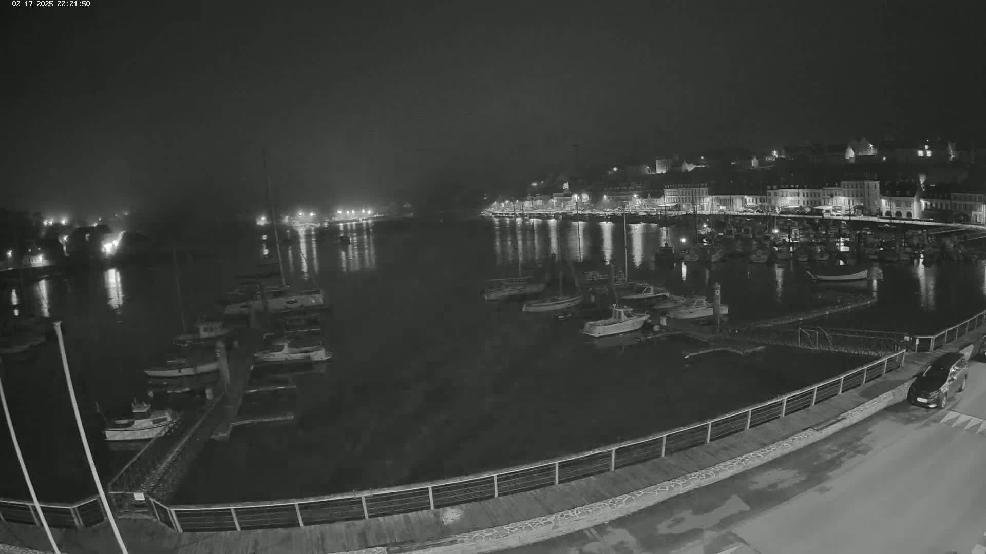 A nighttime, low-light view of a harbor filled with boats, alongside a waterfront town with lights reflecting in the calm water.