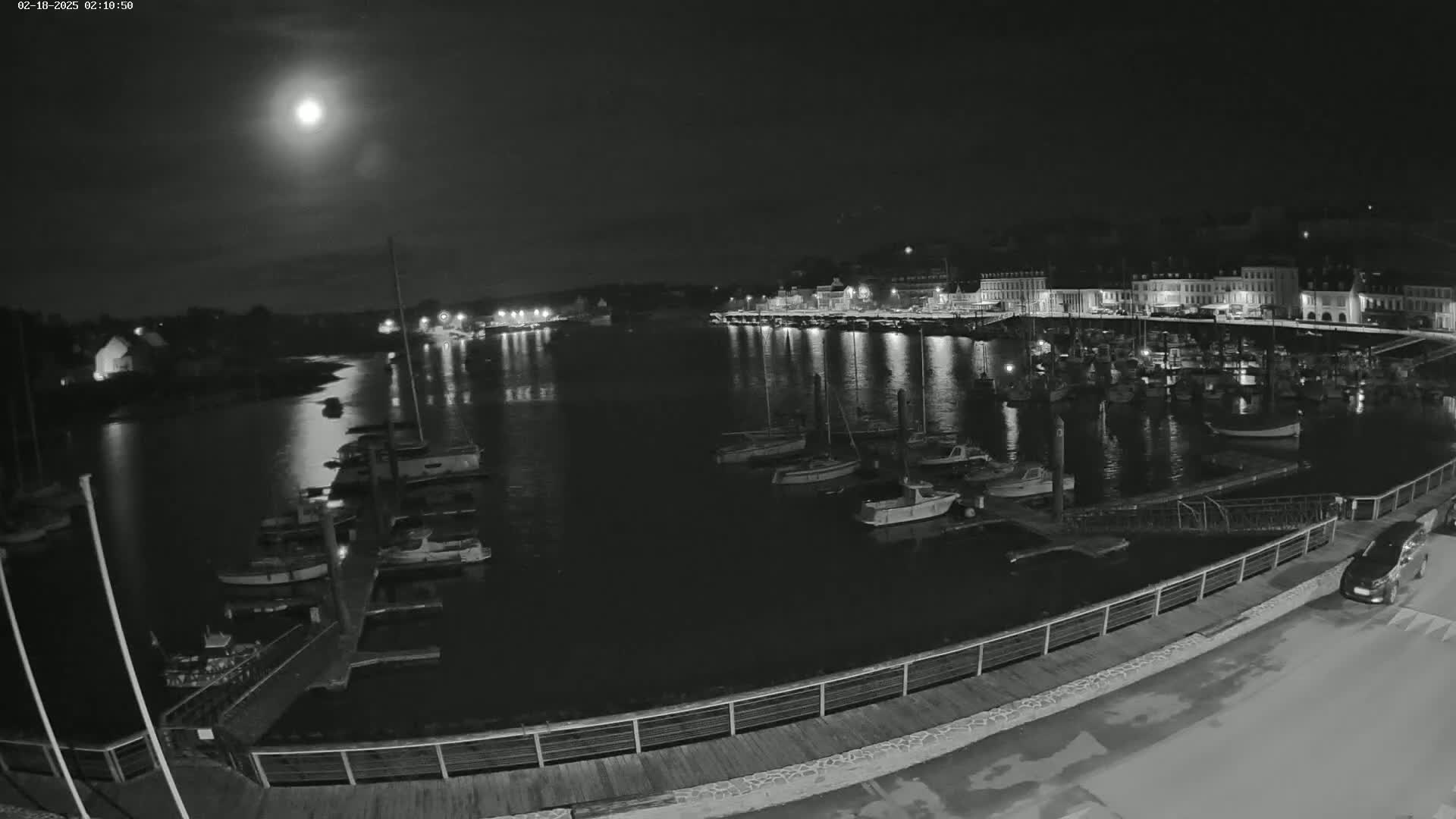 A moonlit night scene shows a harbor filled with boats, alongside a waterfront with buildings and a walkway.