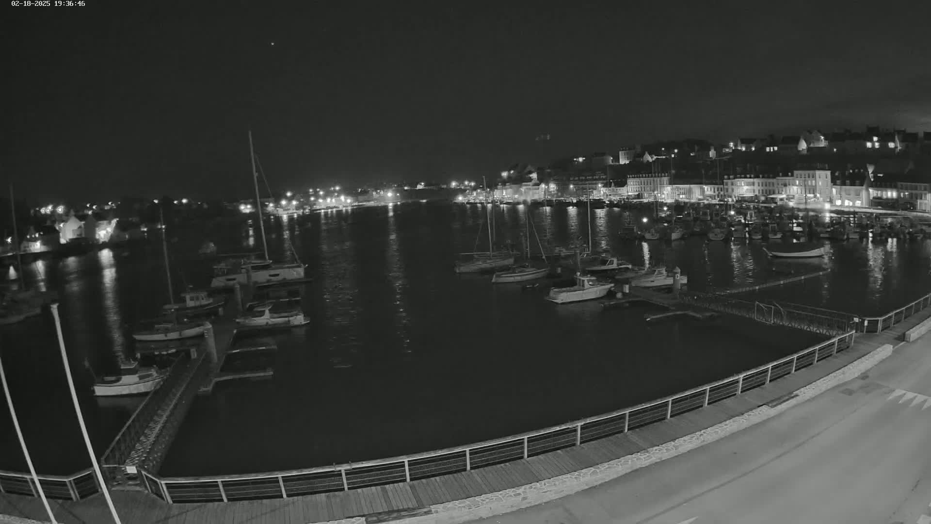 A nighttime view of a harbor filled with boats, docked along a lit waterfront beside a town.