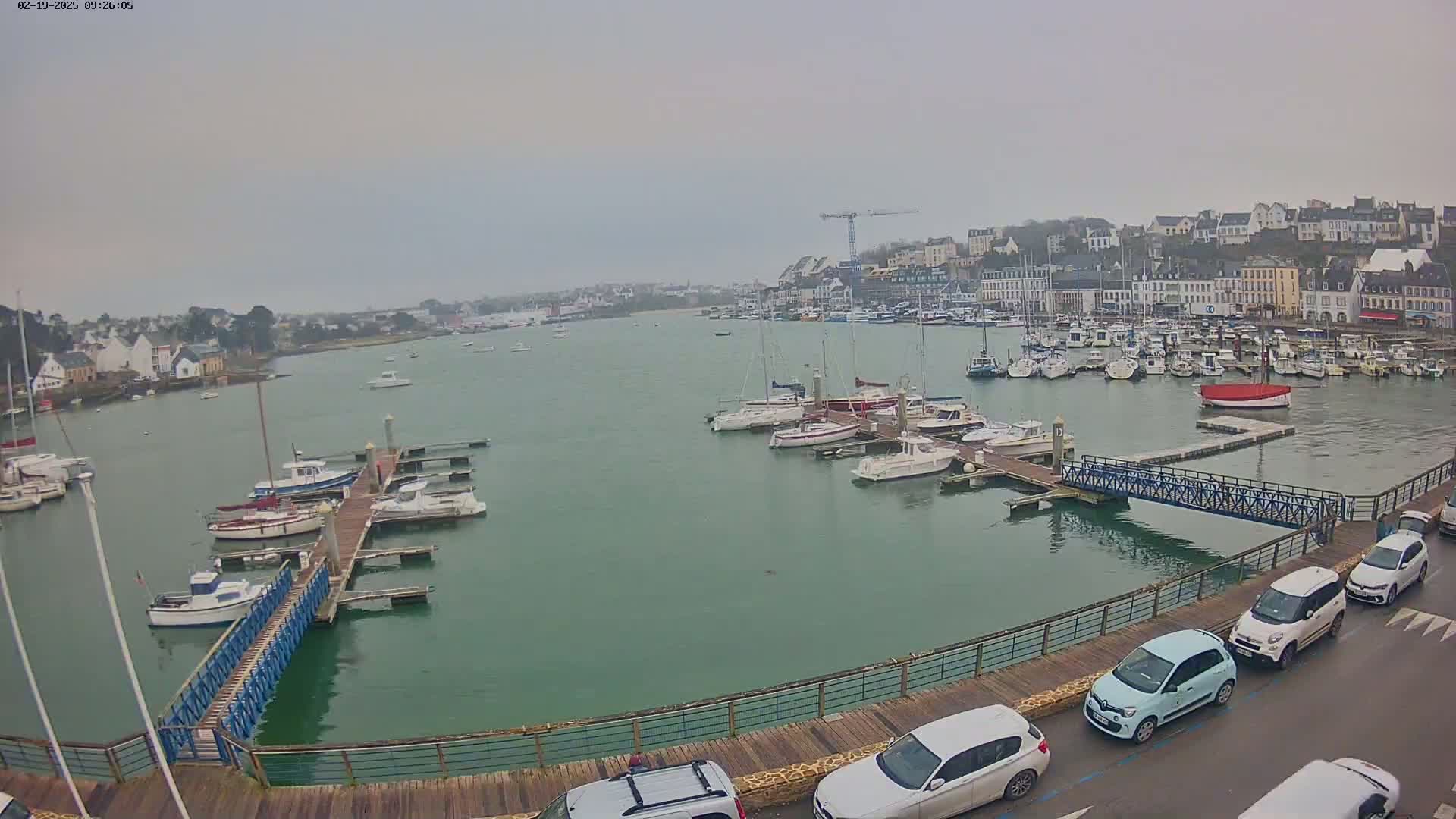 A harbor filled with numerous boats on a cloudy day, with cars parked along a waterfront boardwalk.