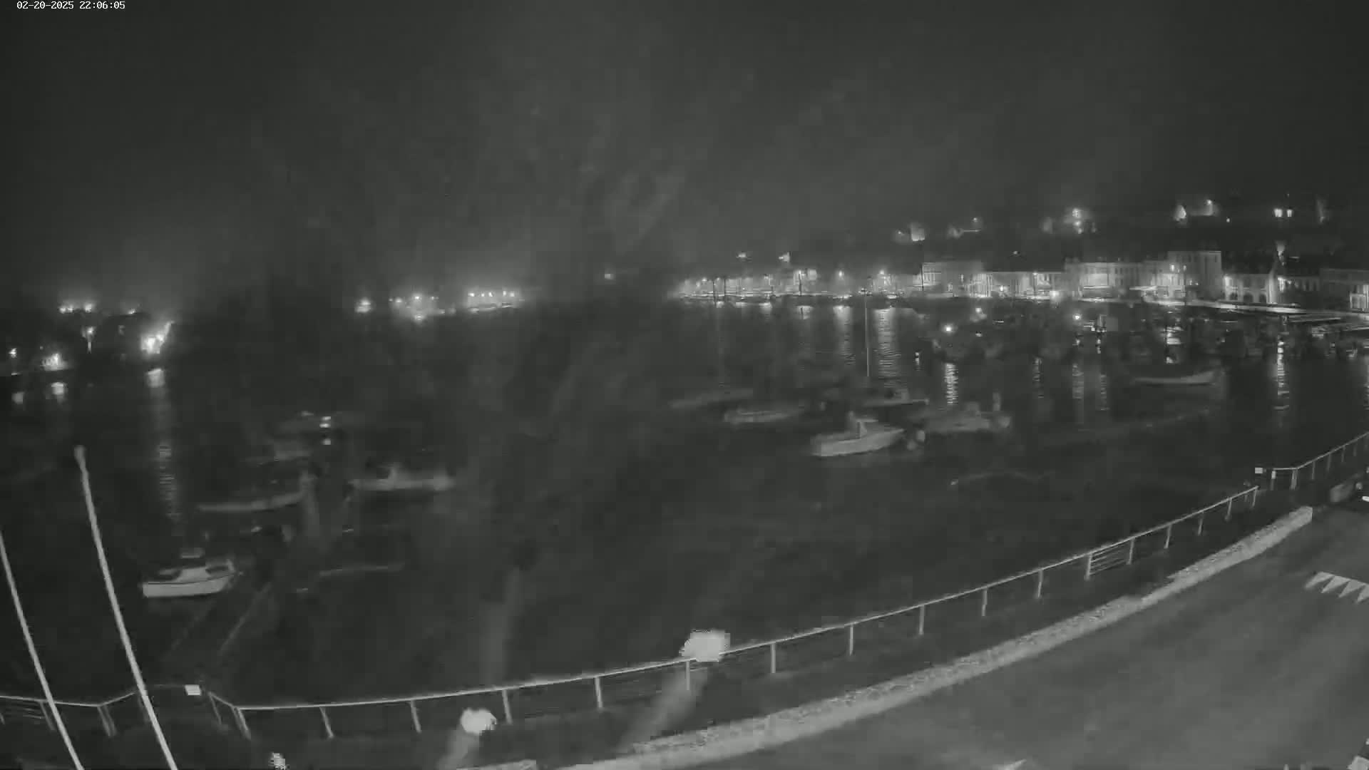 A nighttime, hazy view of a harbor filled with boats and a town with illuminated buildings in the background.