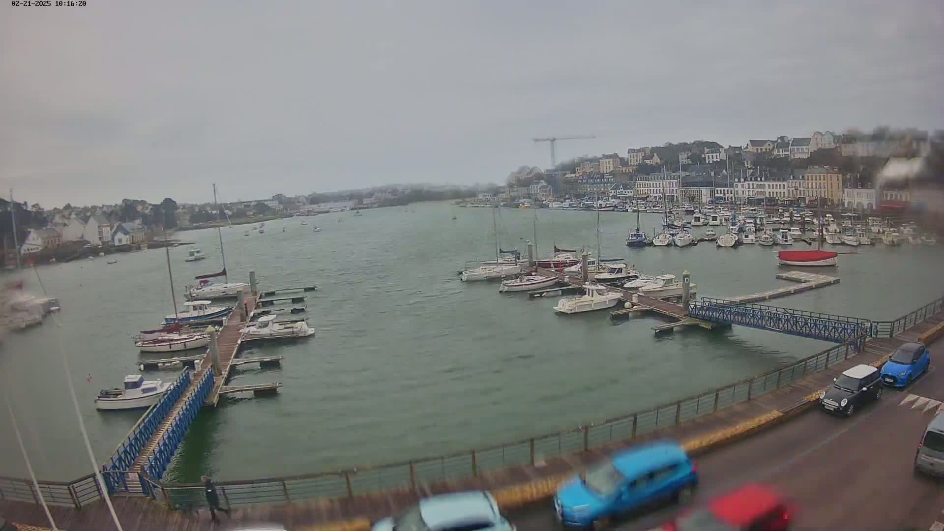 A harbor filled with numerous boats and yachts on a cloudy day, with a town in the background.