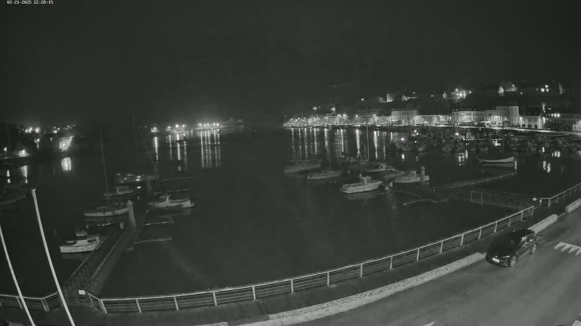 A nighttime view of a harbor filled with boats, with a town's lights reflected in the water.