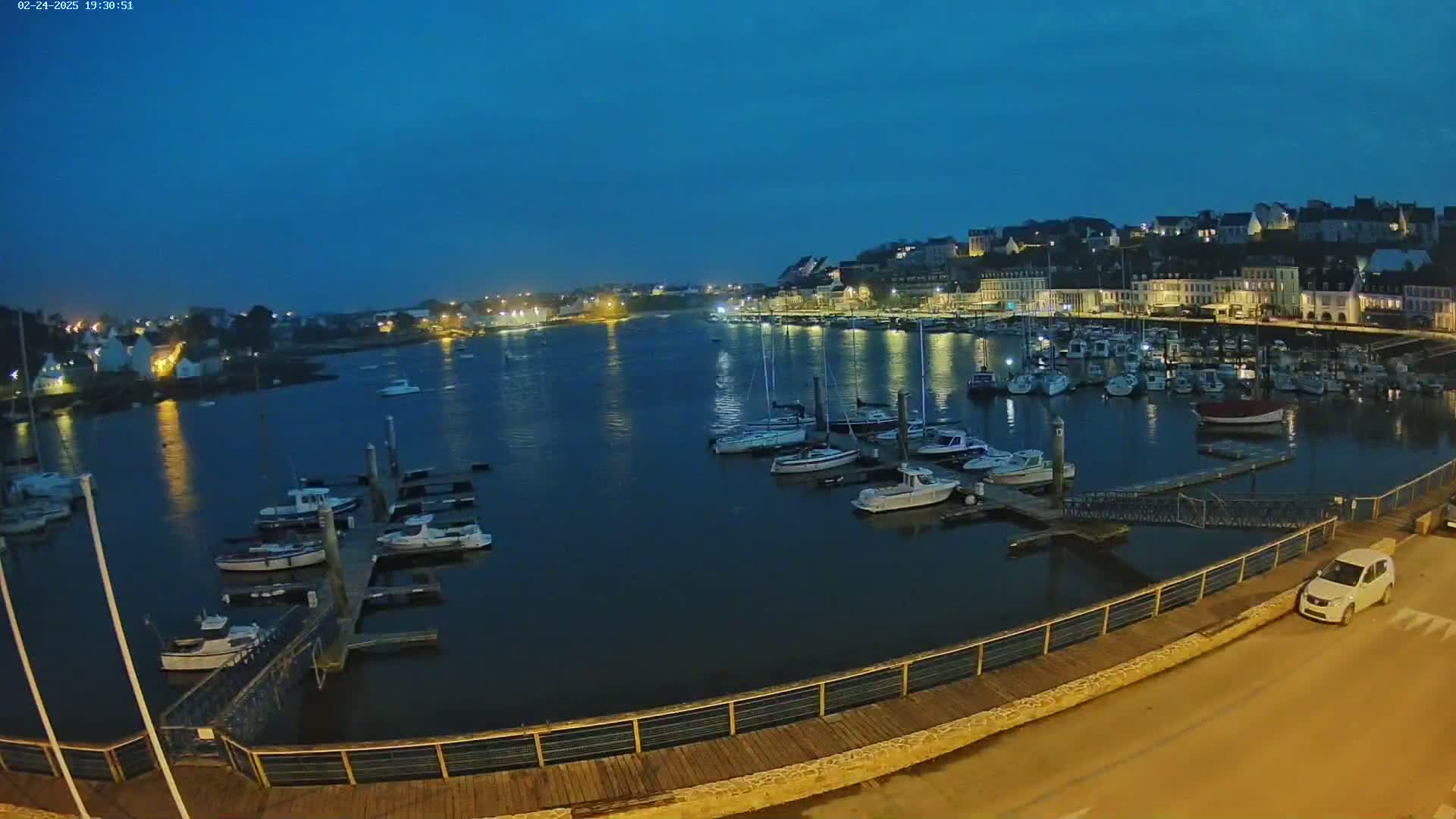 A harbor filled with docked boats at twilight under a clear, dark blue sky.