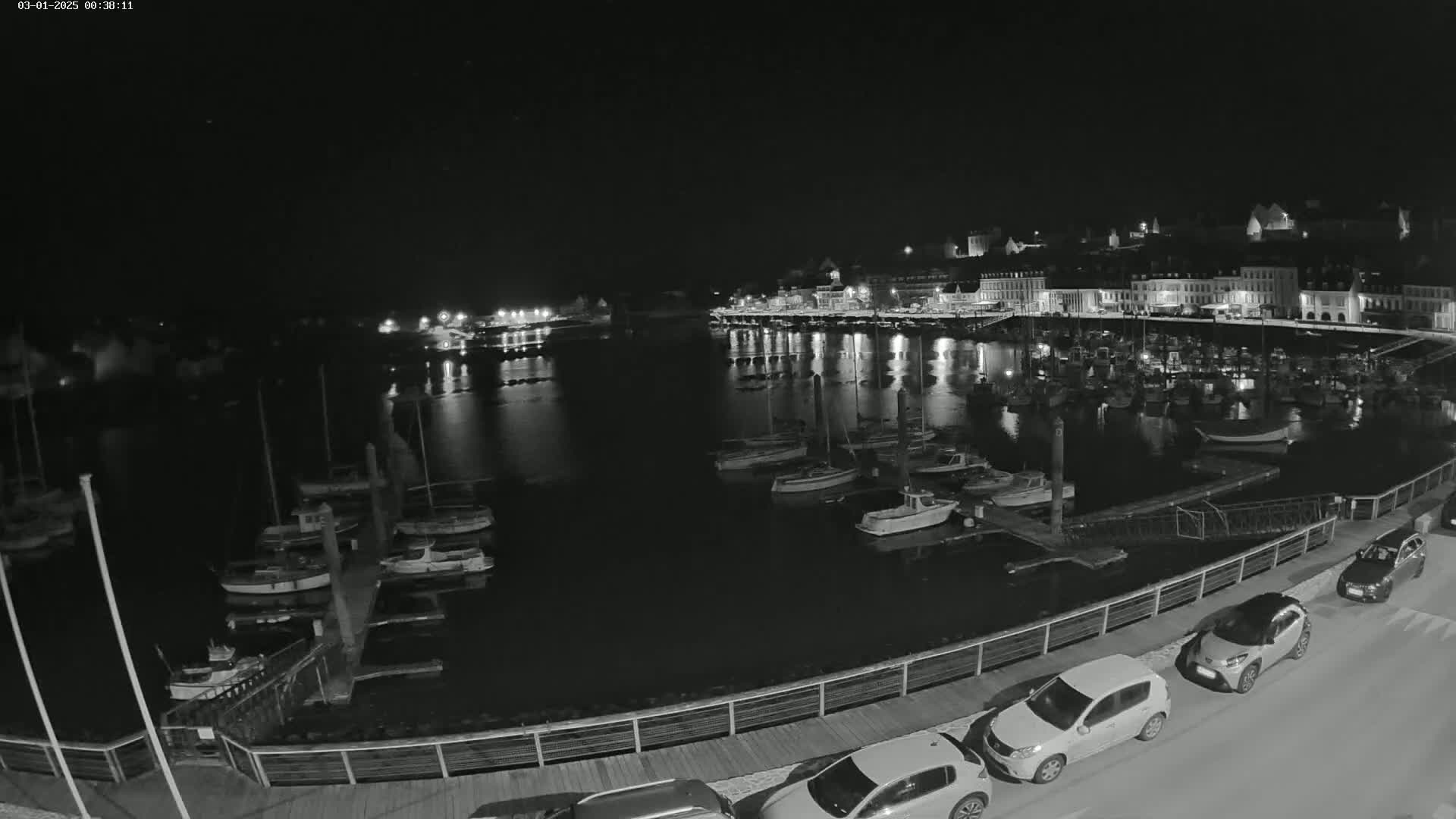 A nighttime, low-light view of a harbor filled with boats, adjacent to a town with lights reflecting on the water.