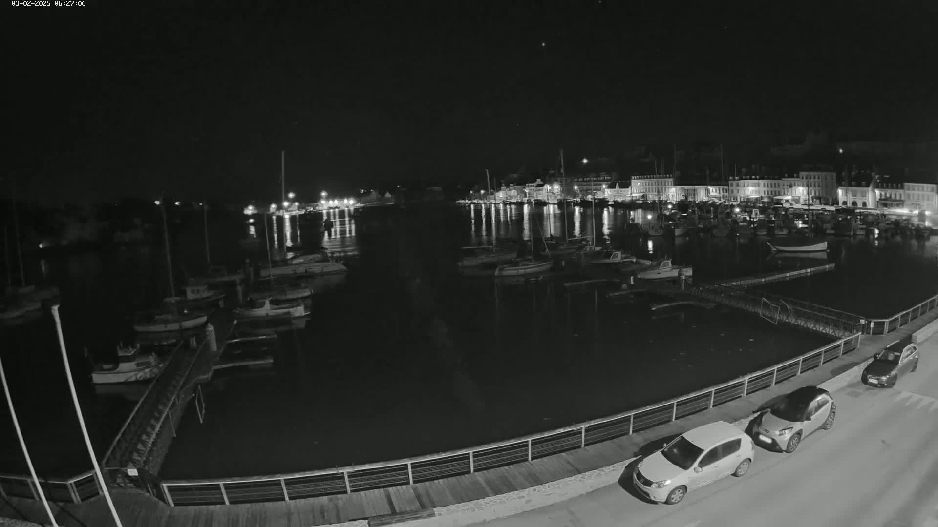 A nighttime view of a harbor filled with boats, illuminated by lights from buildings along the waterfront under a clear, dark sky.