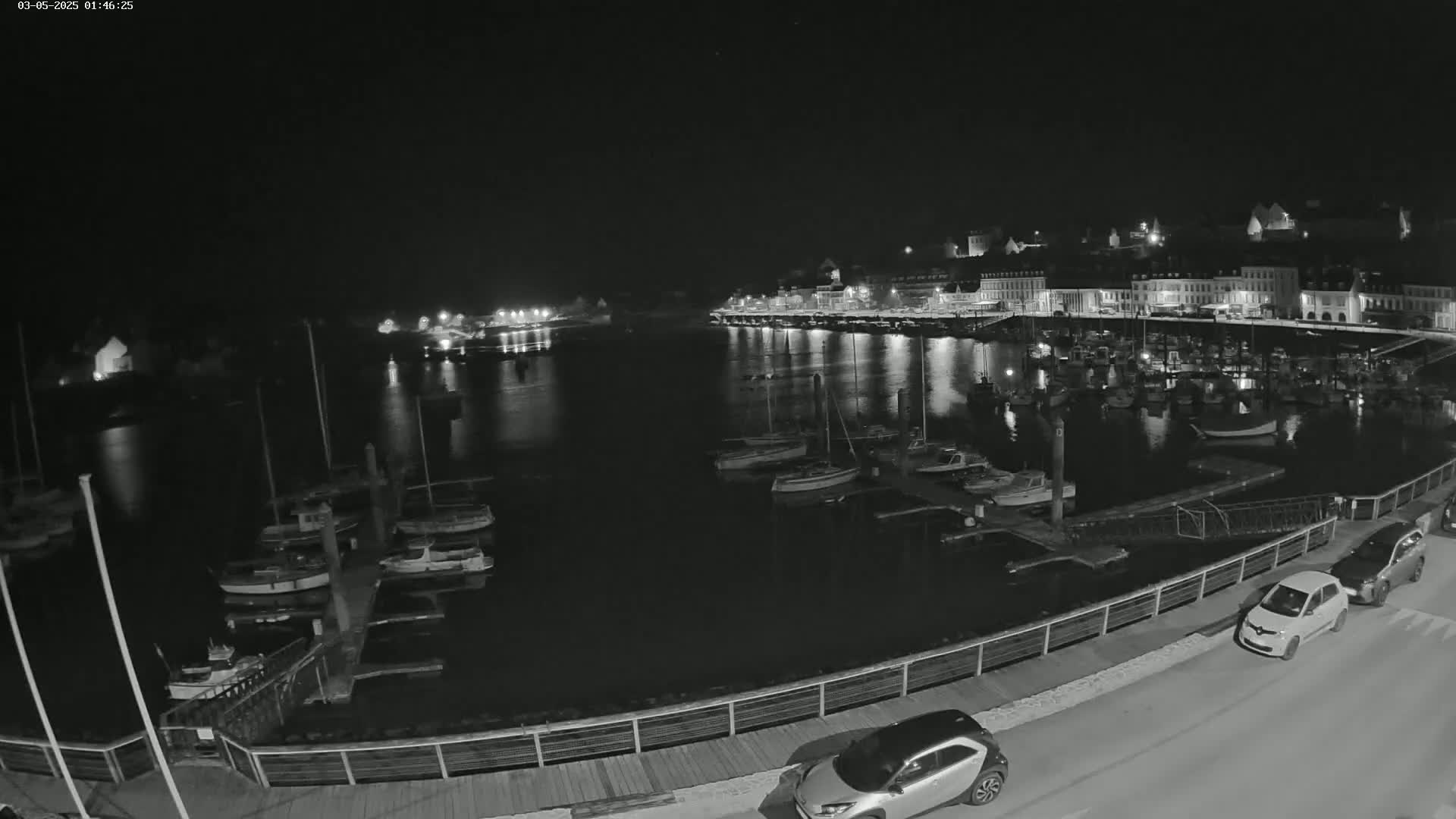A nighttime view of a harbor filled with boats, docked alongside a waterfront town with lights reflecting on the calm water.