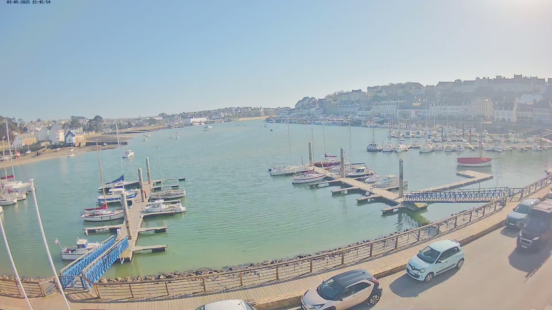A harbor filled with numerous boats and yachts on a sunny day, with a town visible in the background.