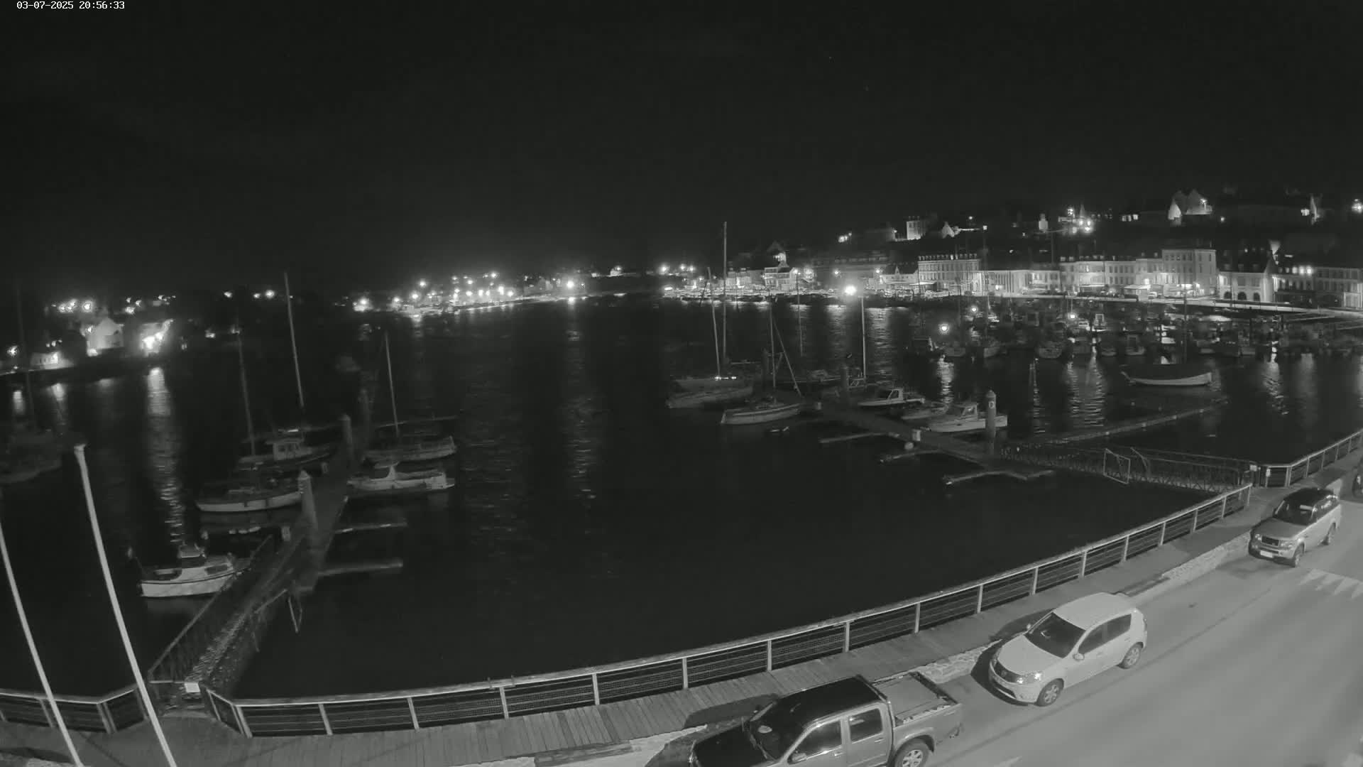 A nighttime, low-light view of a harbor filled with boats, alongside a waterfront town illuminated by streetlights.