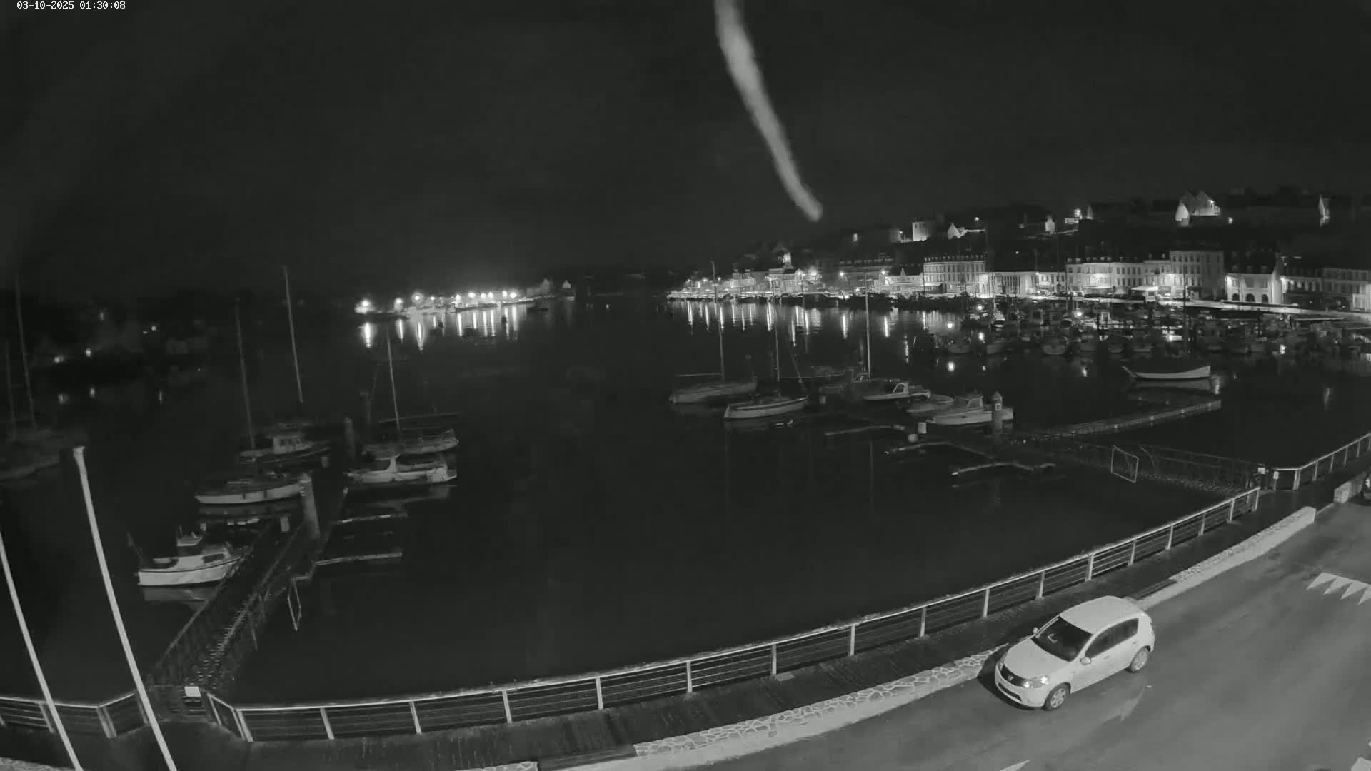 A nighttime view of a harbor filled with boats, alongside a town with illuminated buildings under a dark sky.