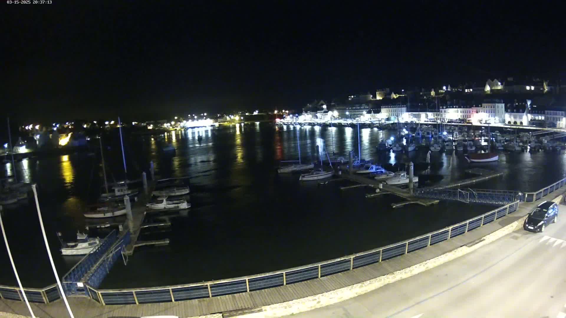 A nighttime view of a harbor filled with boats, docked along a waterfront illuminated by lights from buildings on the shore.