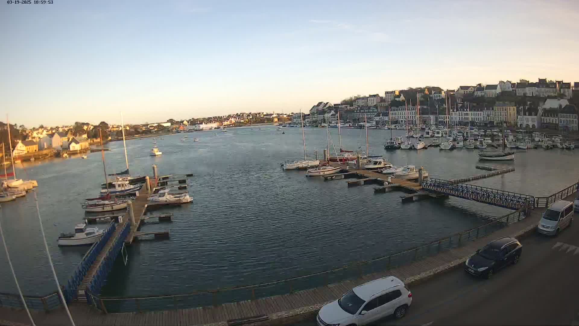 A calm harbor filled with numerous boats and yachts is situated in front of a town under a clear evening sky.