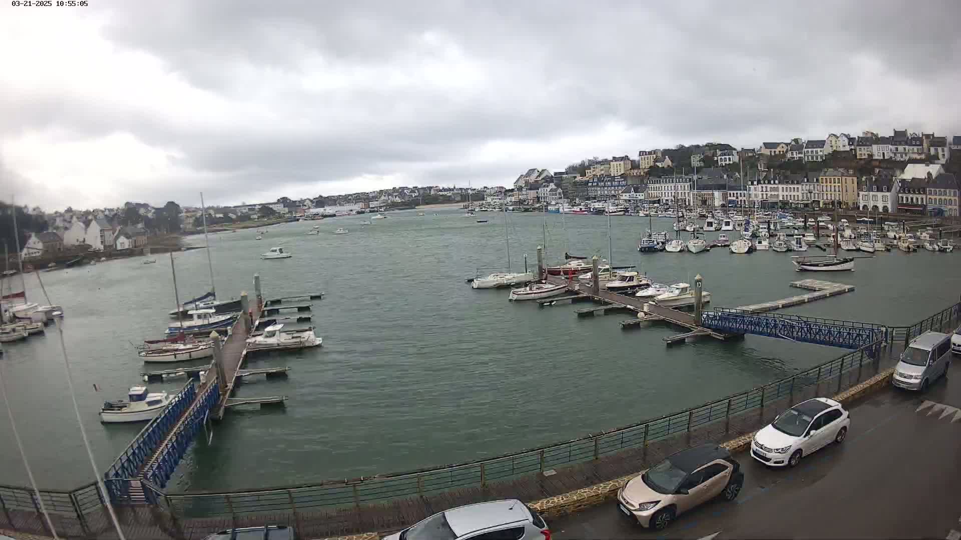 A harbor filled with numerous boats under a cloudy sky, with cars parked along a nearby road.