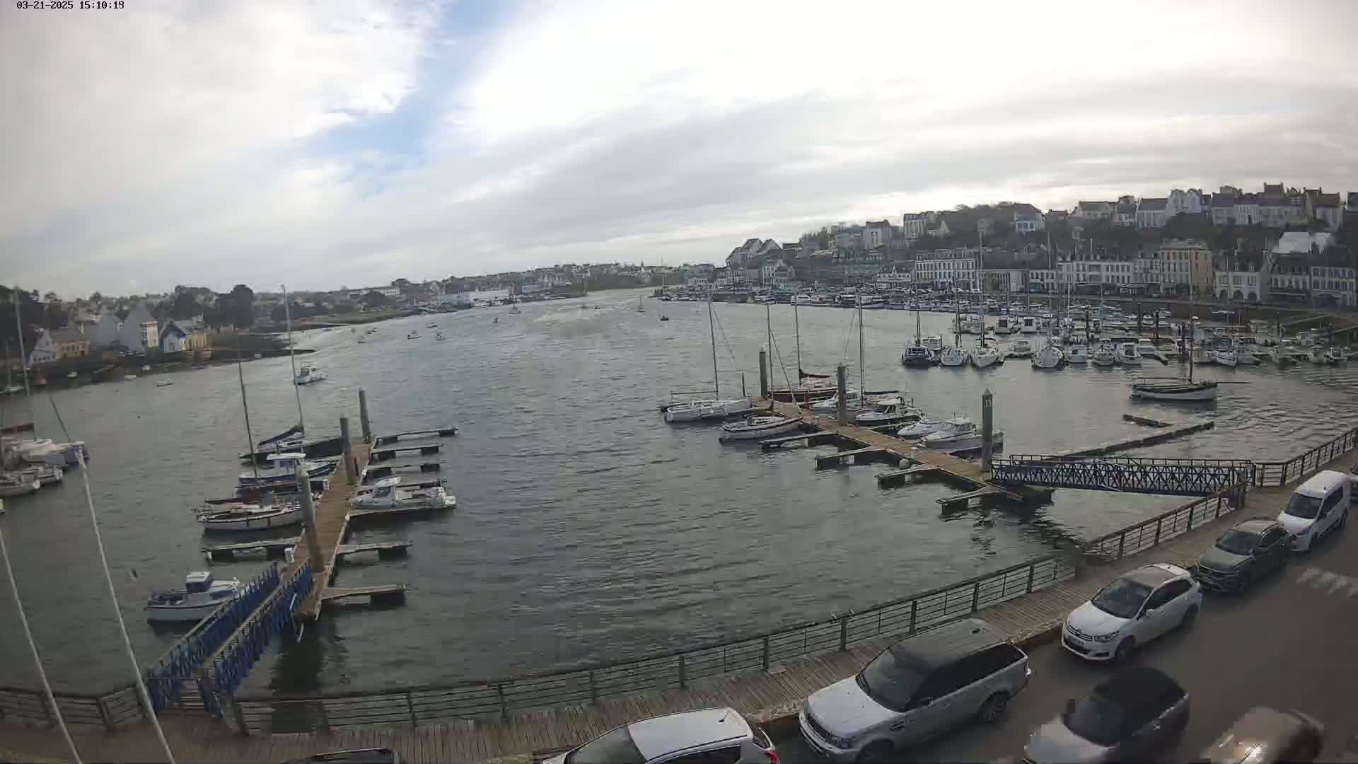 A harbor filled with numerous boats at docks, overlooked by a town under a partly cloudy sky.