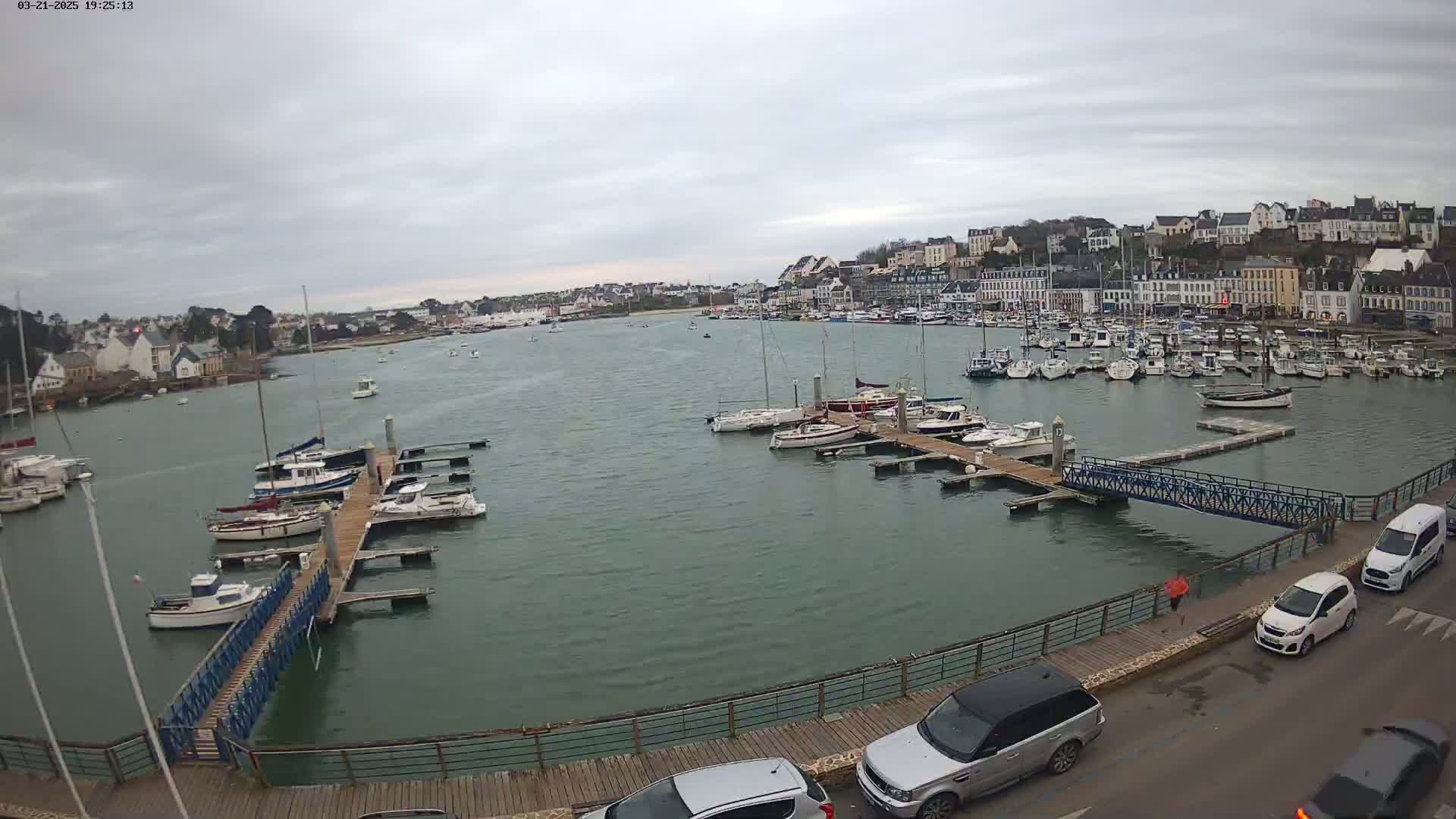 A harbor filled with numerous boats and yachts is overlooked by a town under a cloudy sky.