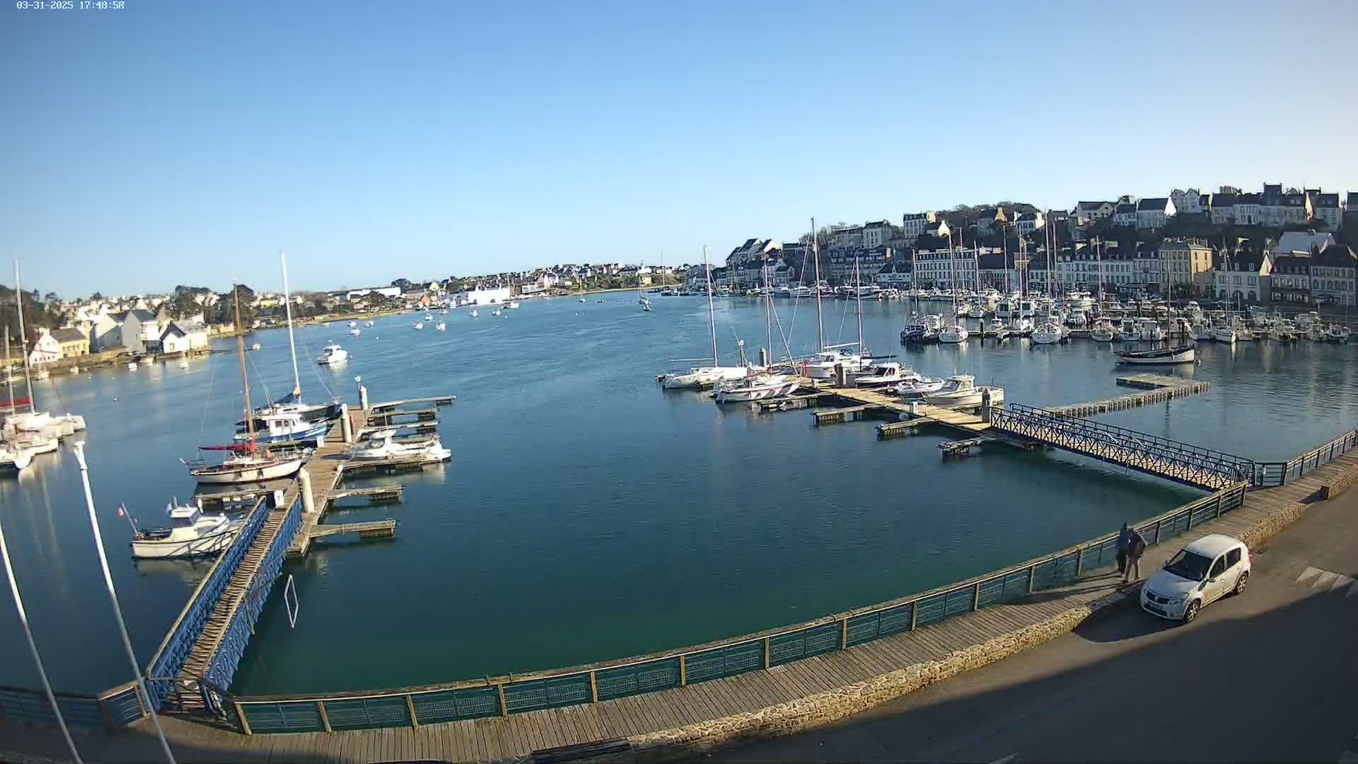 A harbor filled with numerous boats and yachts under a clear blue sky, with a town visible in the background.