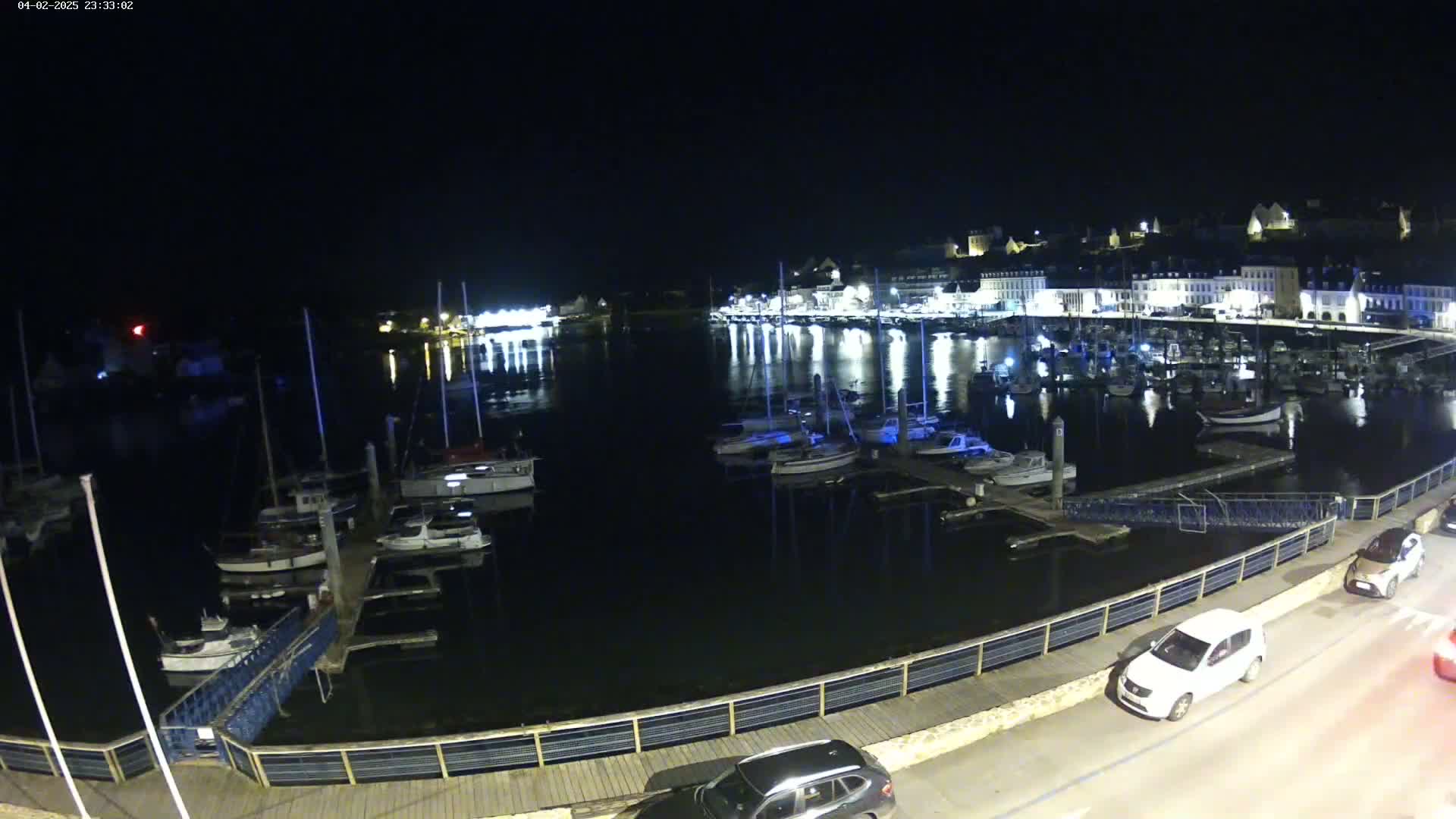 A nighttime view of a harbor filled with boats, docked alongside a waterfront illuminated by lights from buildings in the background.
