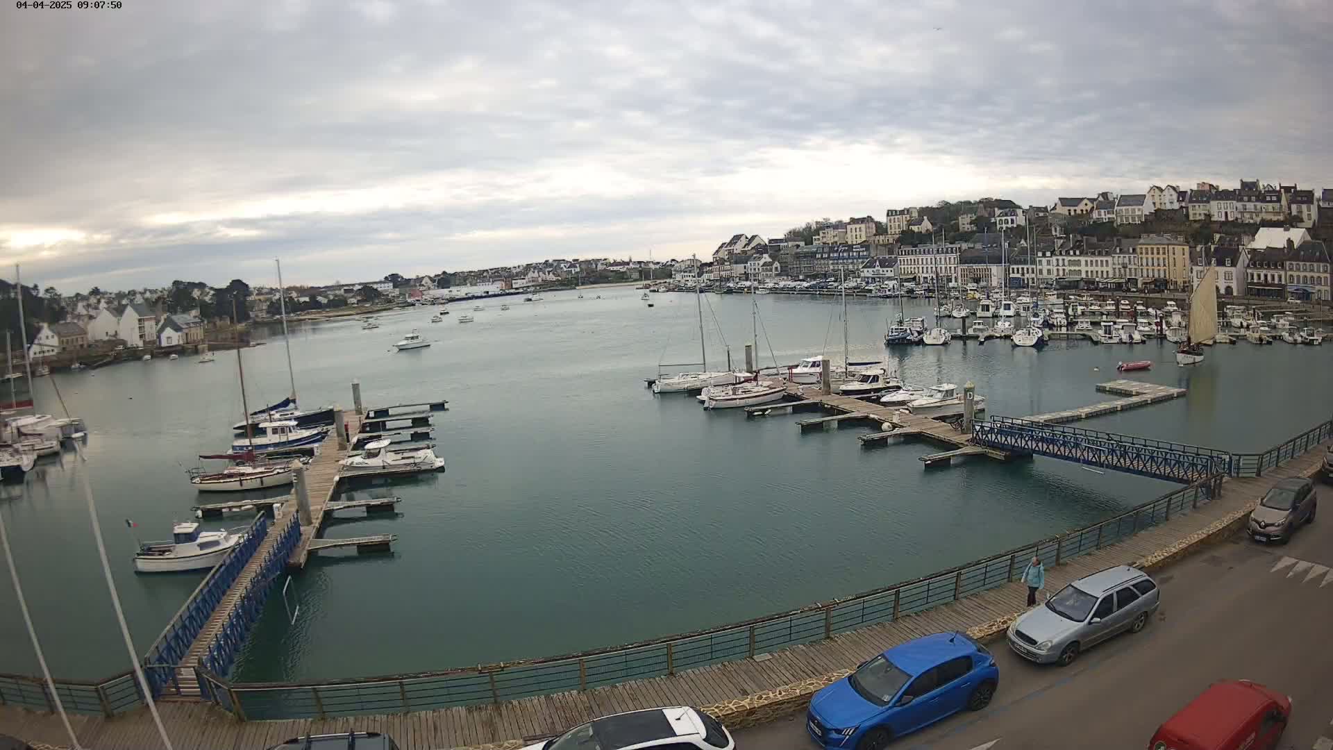 A harbor filled with numerous boats and yachts is situated in front of a town under a cloudy sky.