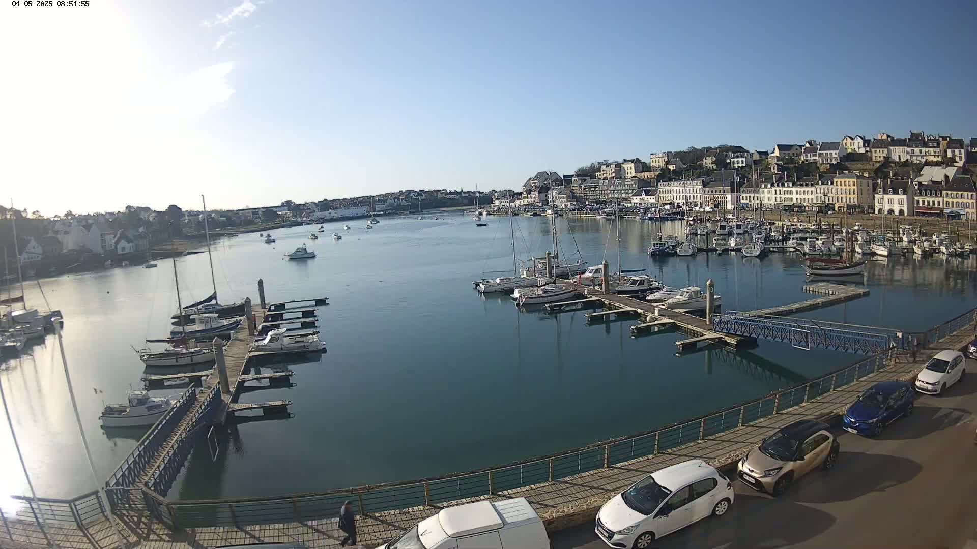 A harbor filled with numerous boats and yachts is situated below a town of buildings on a sunny day.