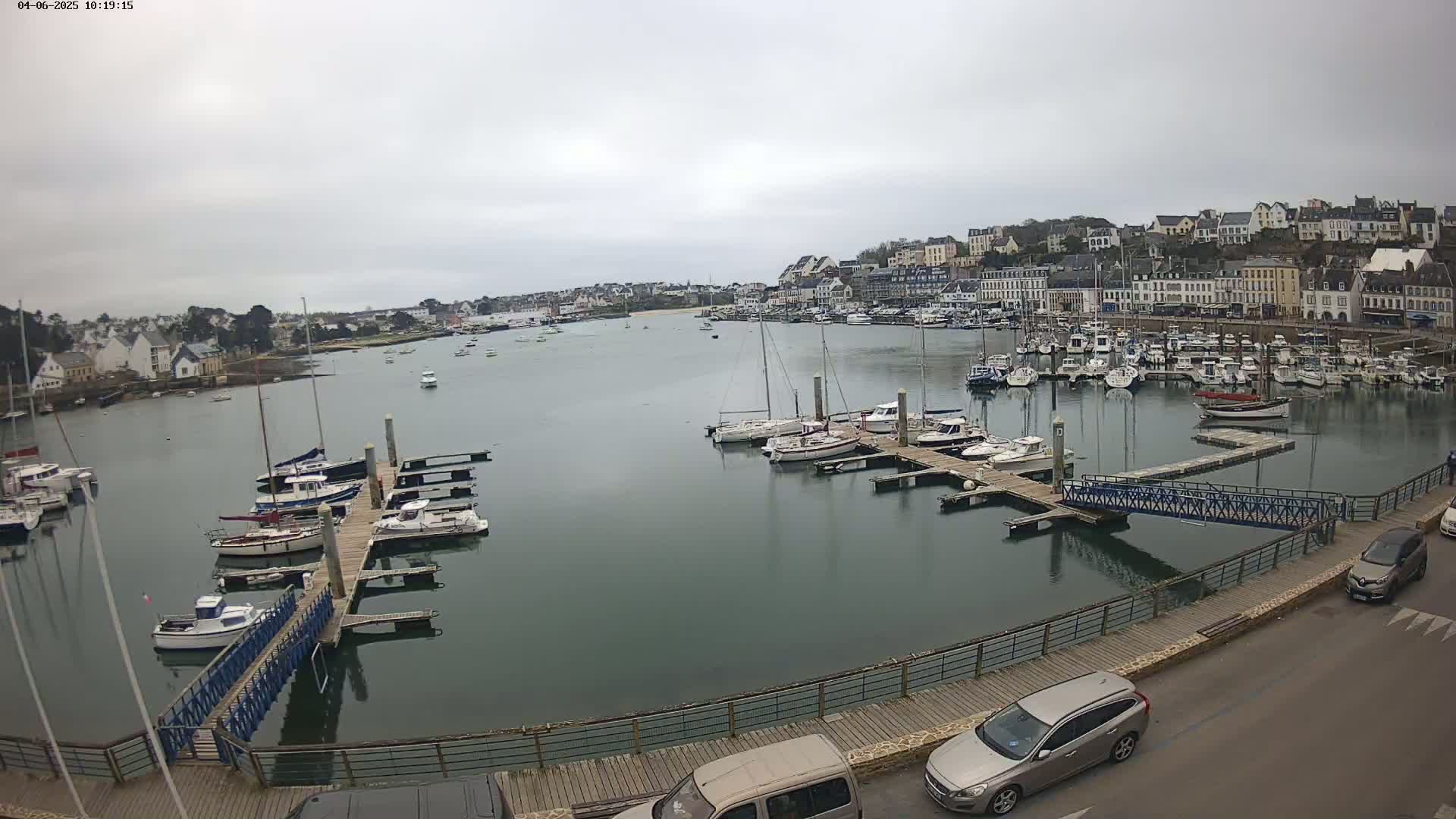 A harbor filled with numerous boats and yachts on a cloudy day, with a town visible in the background.