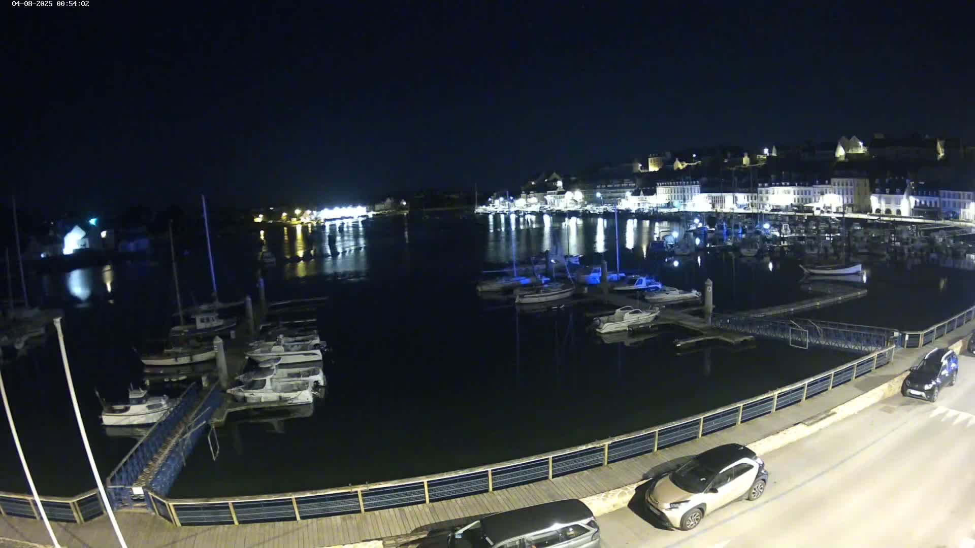 A nighttime view of a harbor filled with boats, illuminated by lights from buildings lining the waterfront under a clear, dark sky.