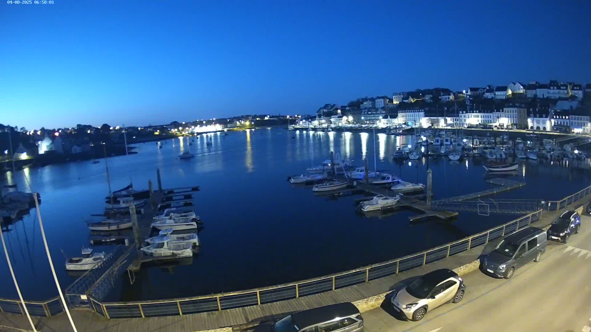 Under a twilight sky, a harbor filled with boats is nestled beside a town of white buildings.