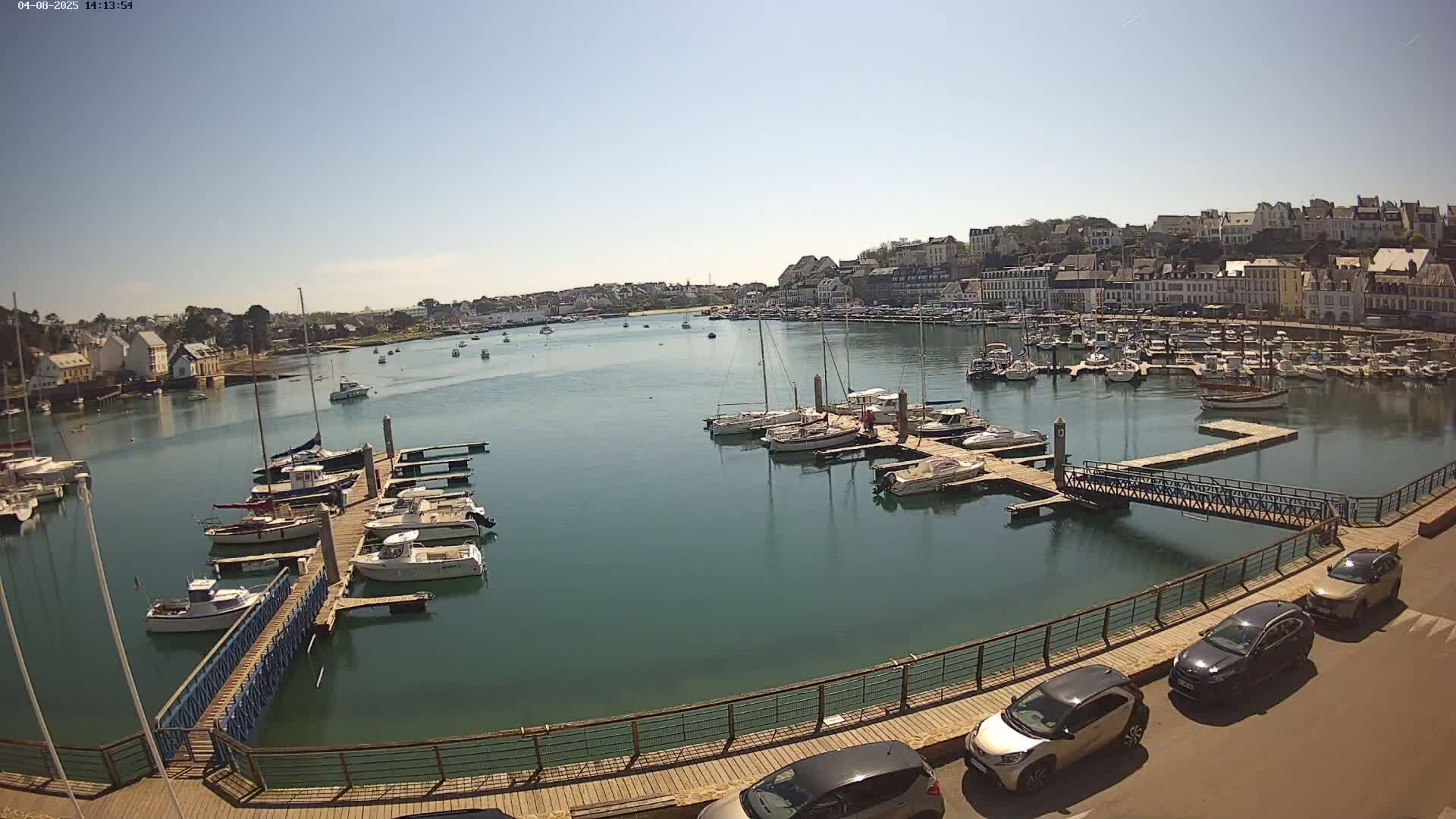 A harbor filled with sailboats and motorboats on a sunny day, overlooked by a town with multi-story buildings.