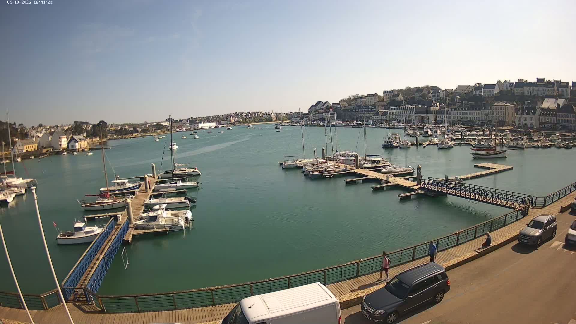 A harbor filled with sailboats and motorboats on a sunny day, with a town in the background.