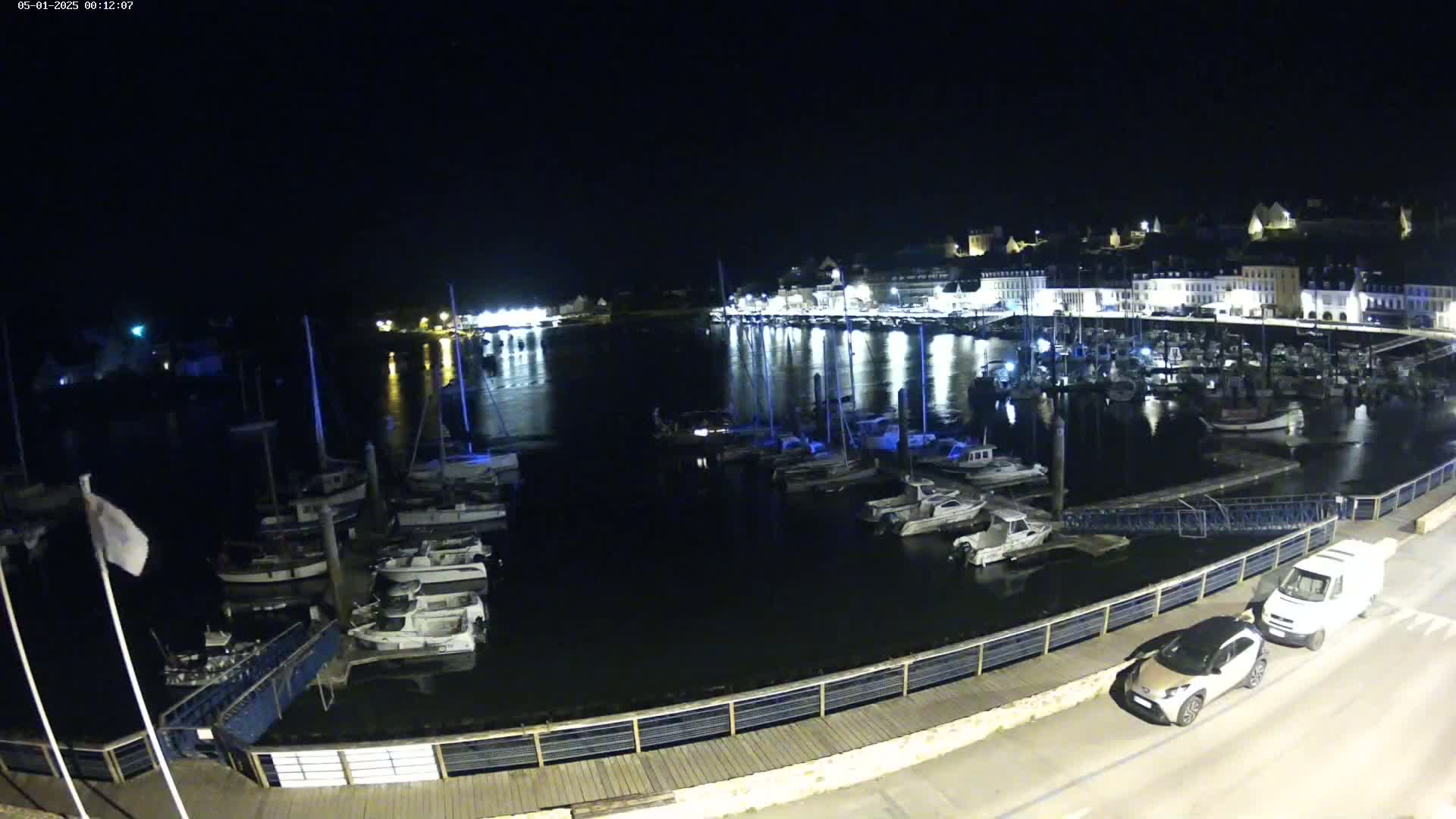 A nighttime view of a harbor filled with boats, reflecting the lights of a town on the opposite shore.