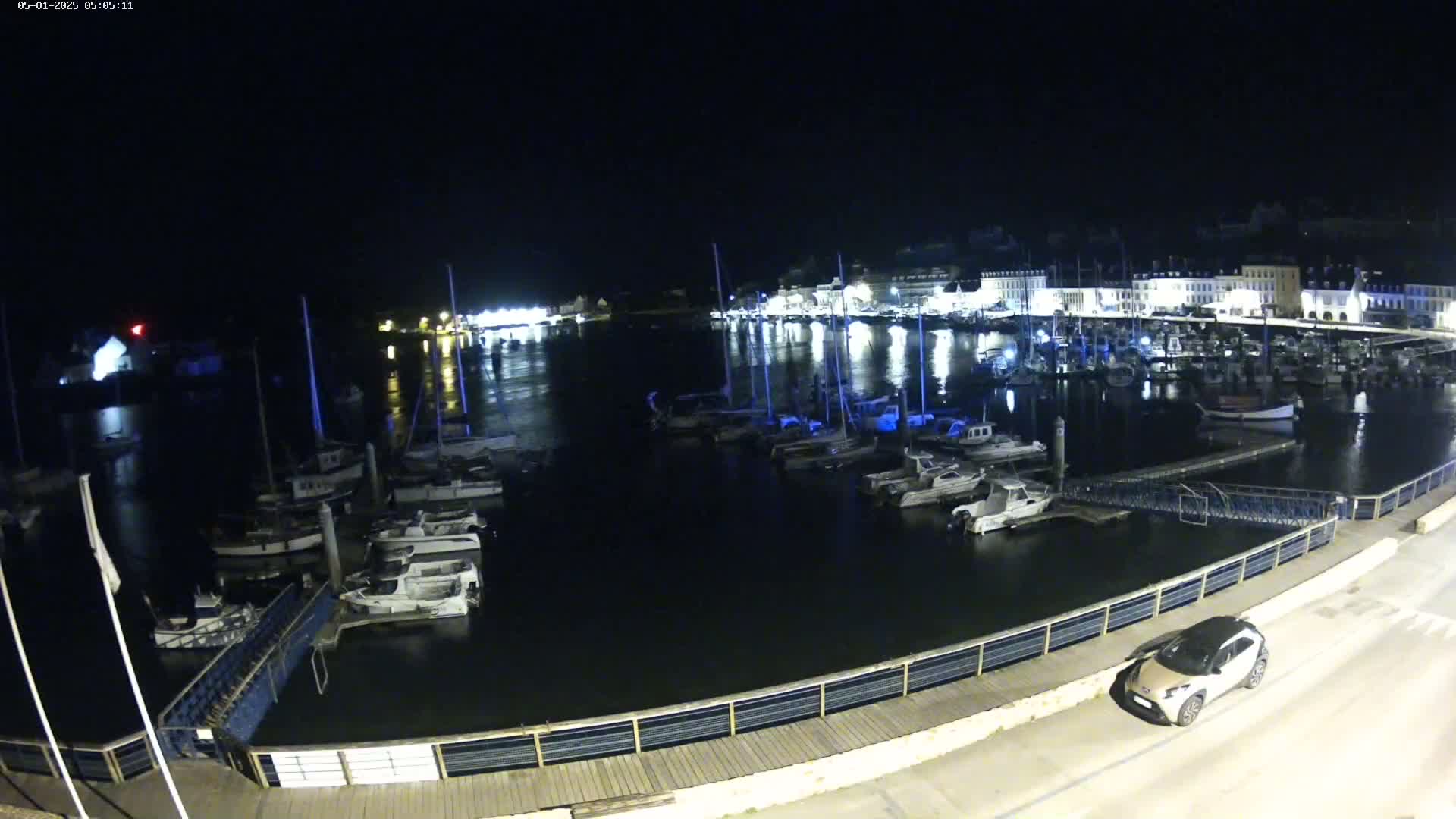 A nighttime view of a harbor filled with boats, illuminated by lights from buildings along the shoreline.