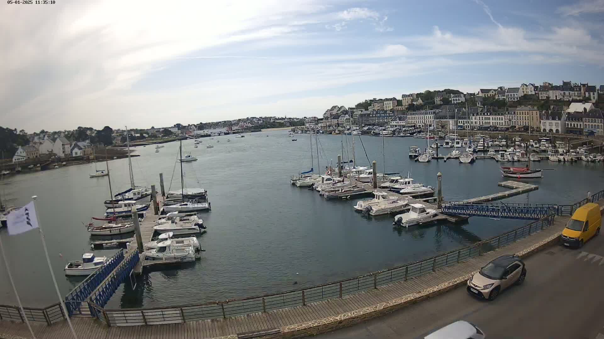 A harbor filled with numerous boats and yachts is situated in front of a town under a partly cloudy sky.