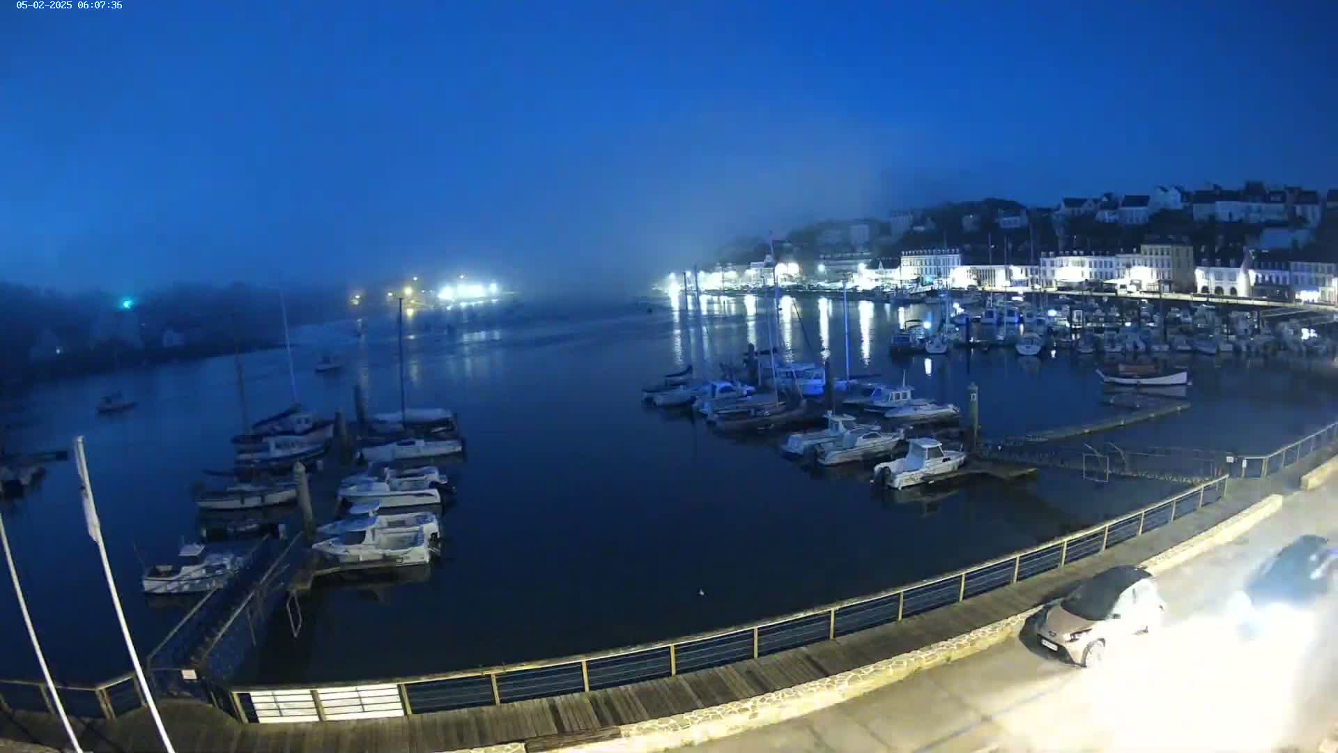 Many boats are moored in a harbor at twilight under a mostly clear, dark blue sky.