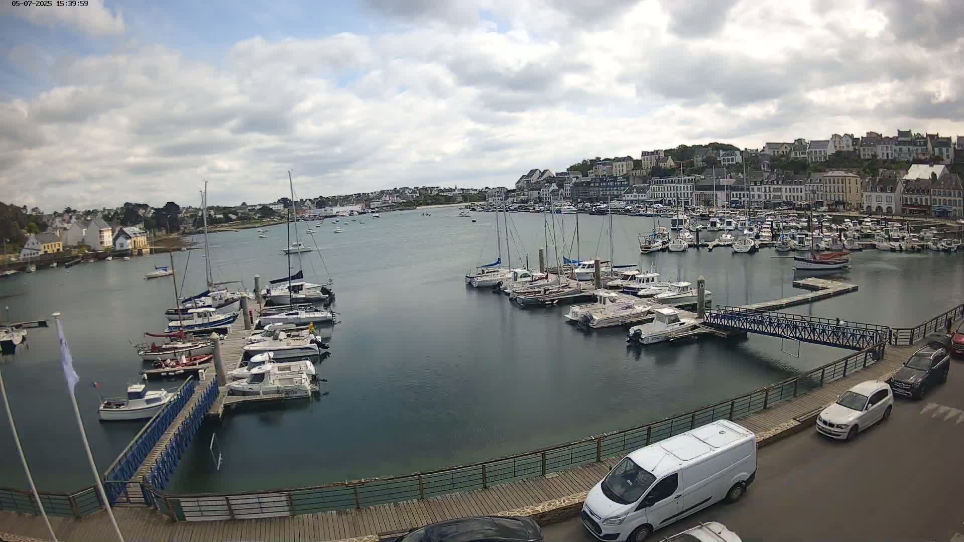 A harbor filled with sailboats and motorboats is viewed from a slightly elevated position on a partly cloudy day.