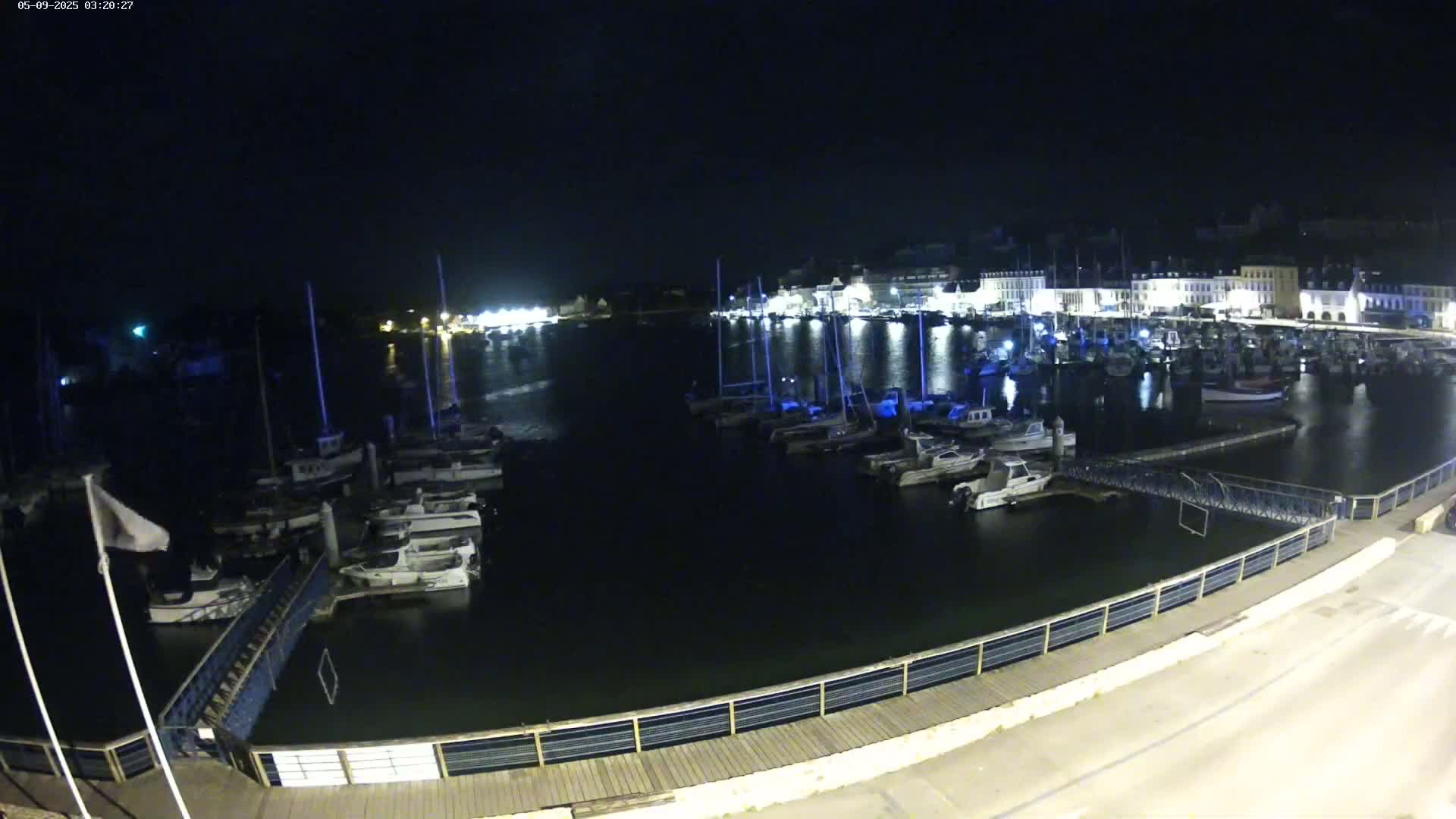 A nighttime view of a harbor filled with boats, docked alongside a waterfront with buildings illuminated in the background.