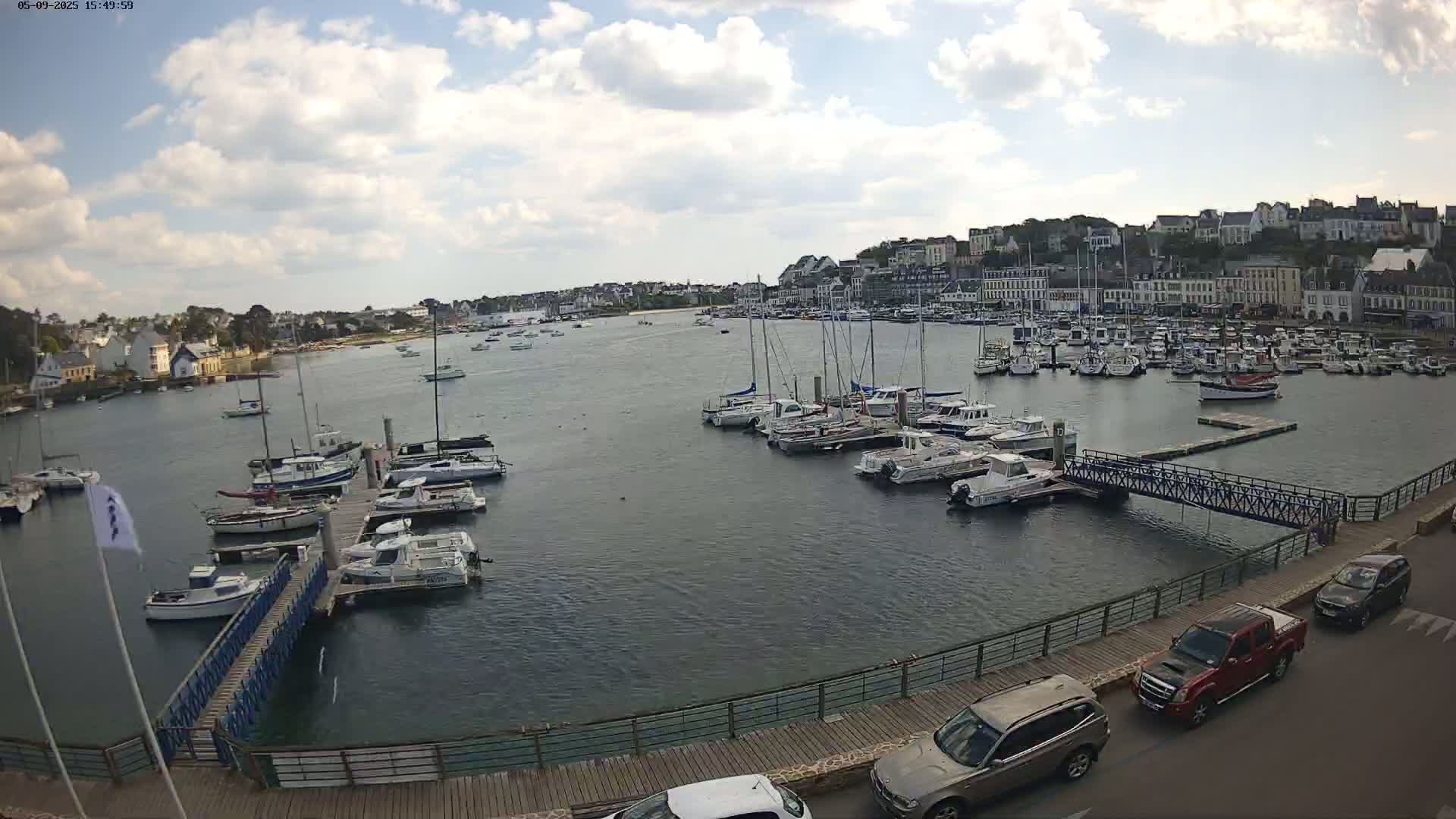A harbor filled with numerous boats and yachts is situated near a town under a partly cloudy sky.