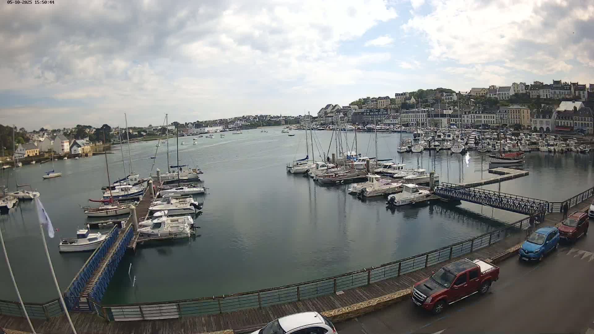 A harbor filled with numerous boats and yachts under a partly cloudy sky, with a town visible in the background.