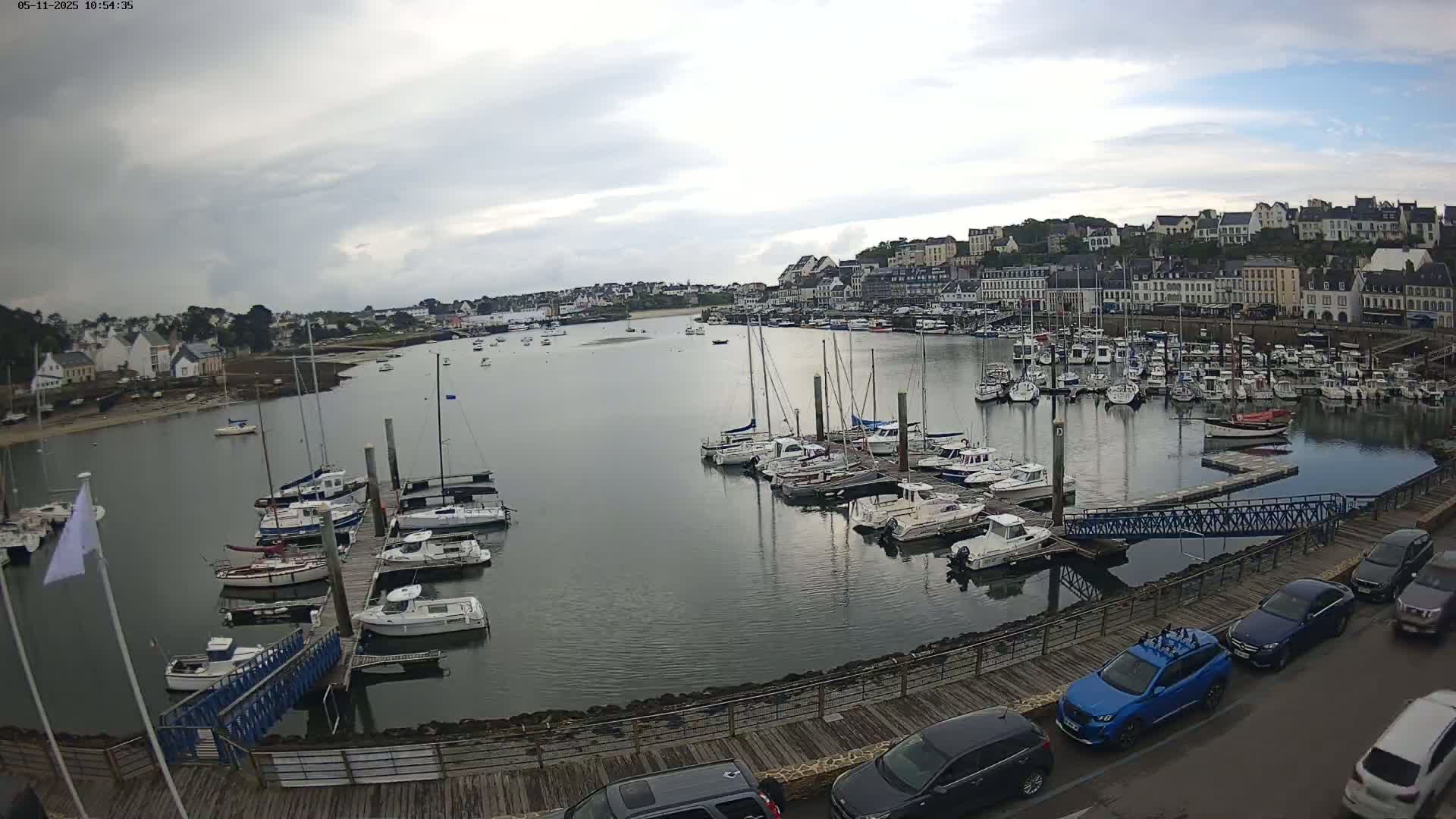 A harbor filled with numerous sailboats and motorboats is situated next to a town under a mostly cloudy sky.