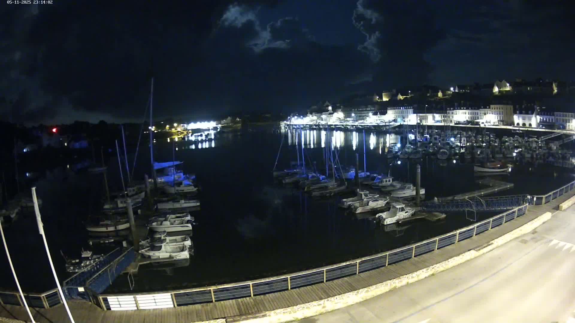 A nighttime harbor filled with boats and illuminated buildings under a partly cloudy sky.