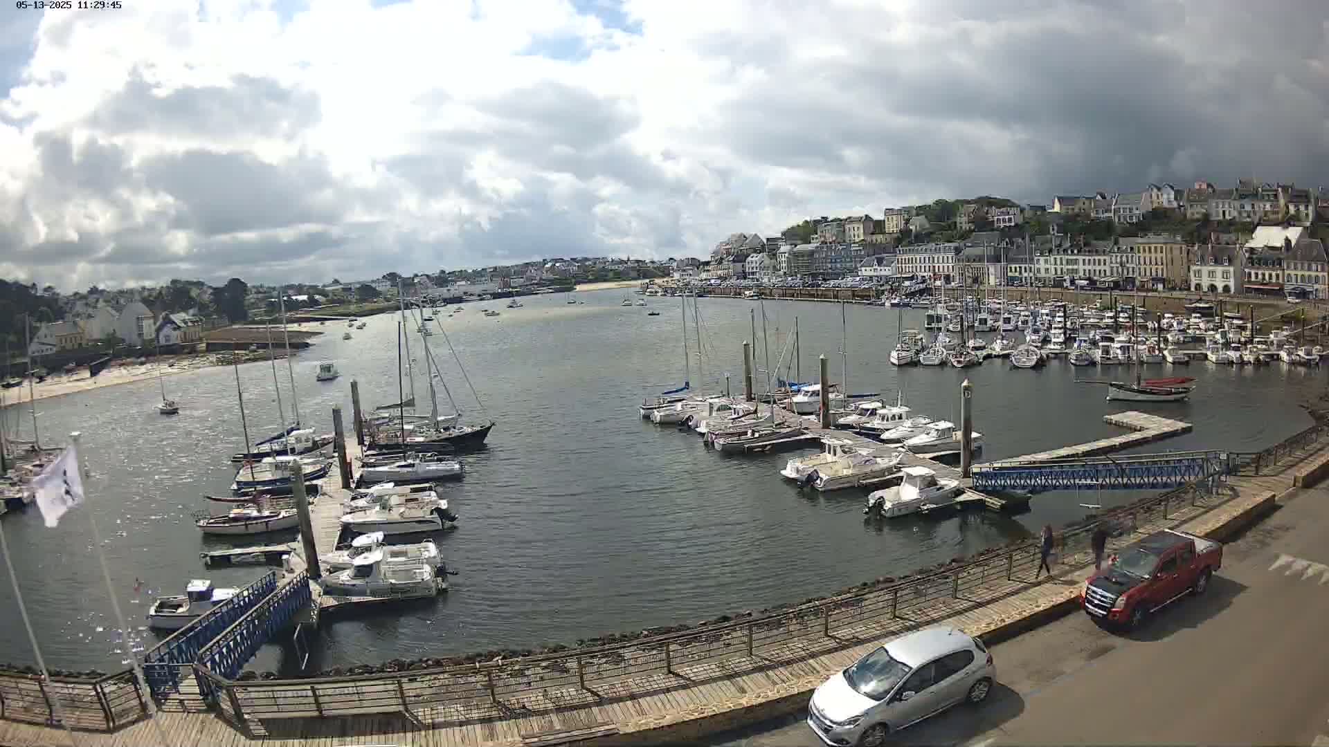 A harbor filled with numerous sailboats and motorboats is overlooked by a town under a partly cloudy sky.
