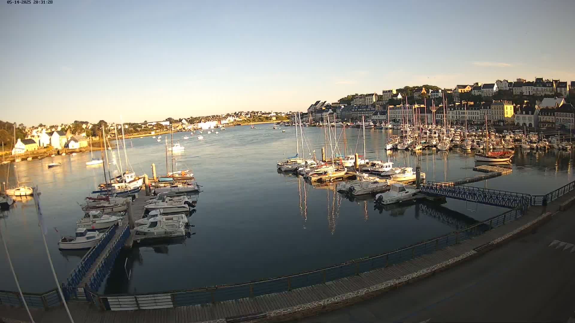 A calm harbor filled with numerous boats at sunset, overlooked by a town.
