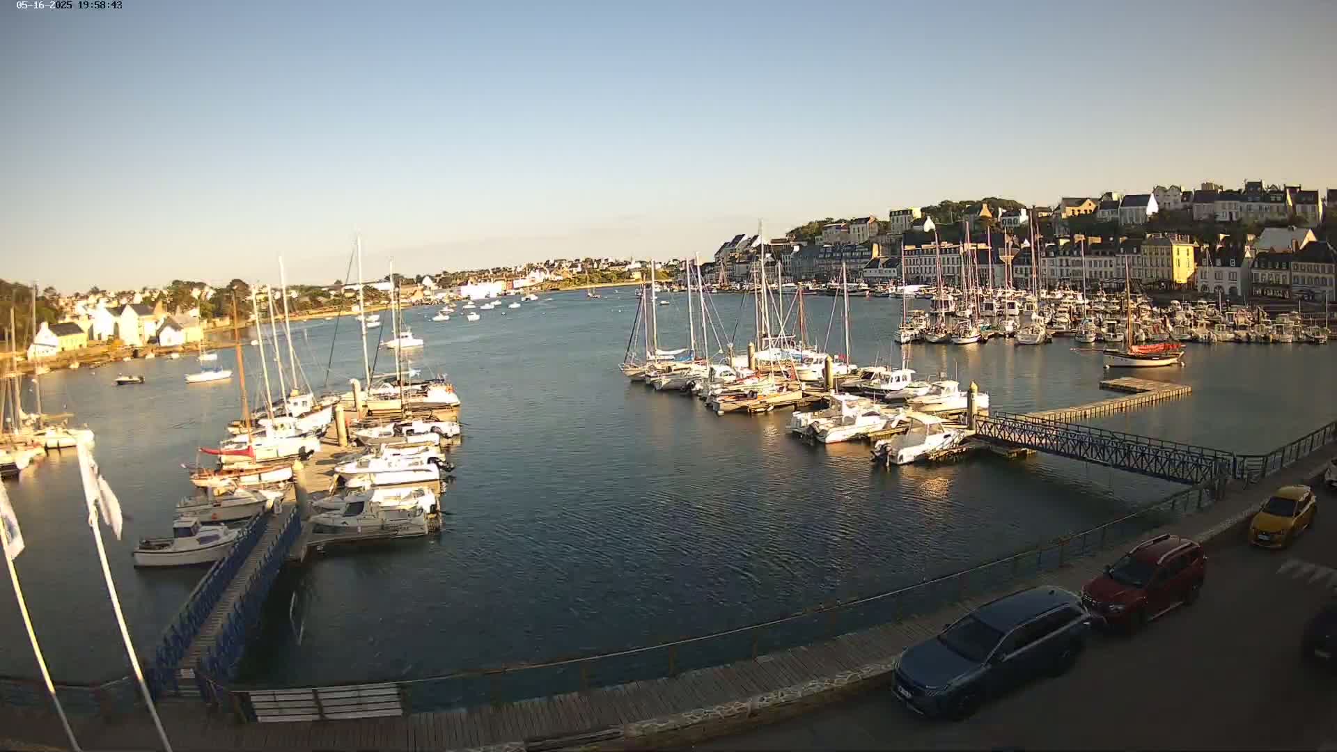 A harbor filled with sailboats and motorboats is nestled beside a town under a clear, sunny sky.