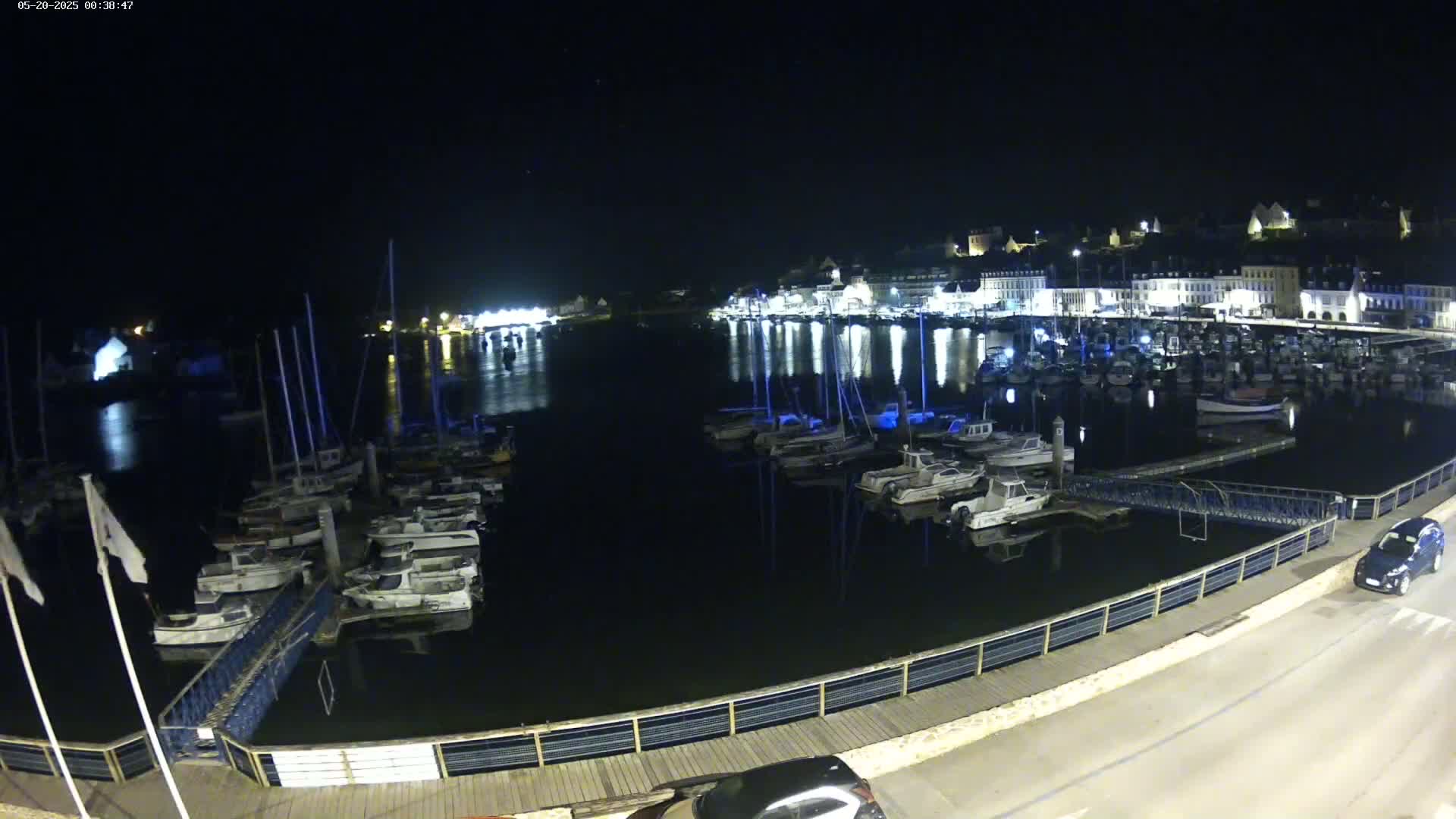 A nighttime view of a harbor filled with docked boats, illuminated by lights from buildings on the shore.