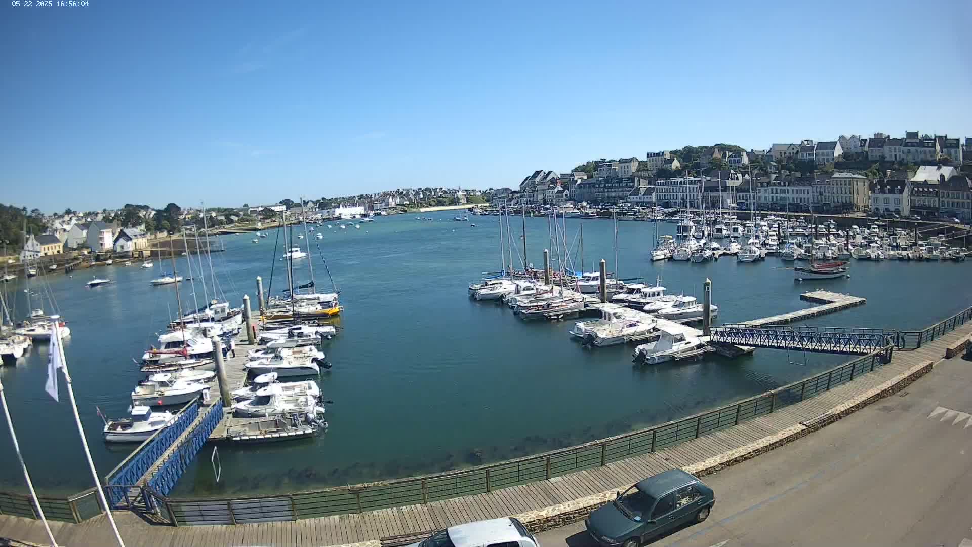 A harbor filled with numerous sailboats and motorboats on a sunny day, with a town visible in the background.