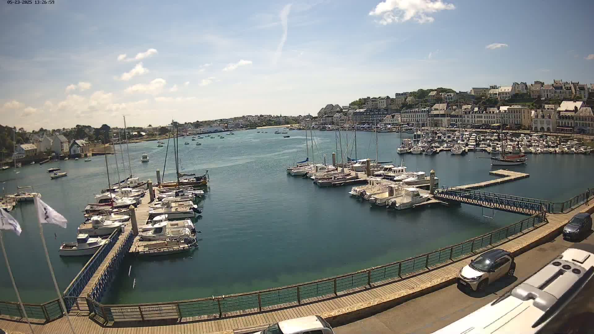 A harbor filled with numerous boats and yachts on a sunny day, with a town in the background.