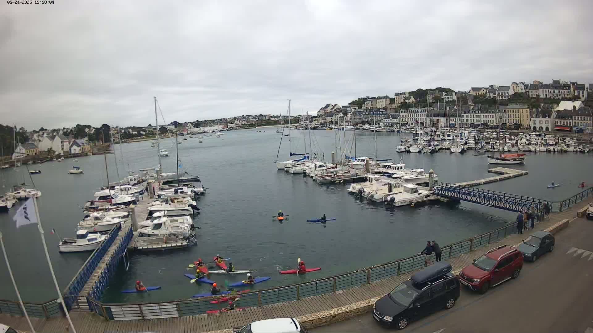 Kayakers paddle in a harbor filled with numerous boats and yachts, under an overcast sky.